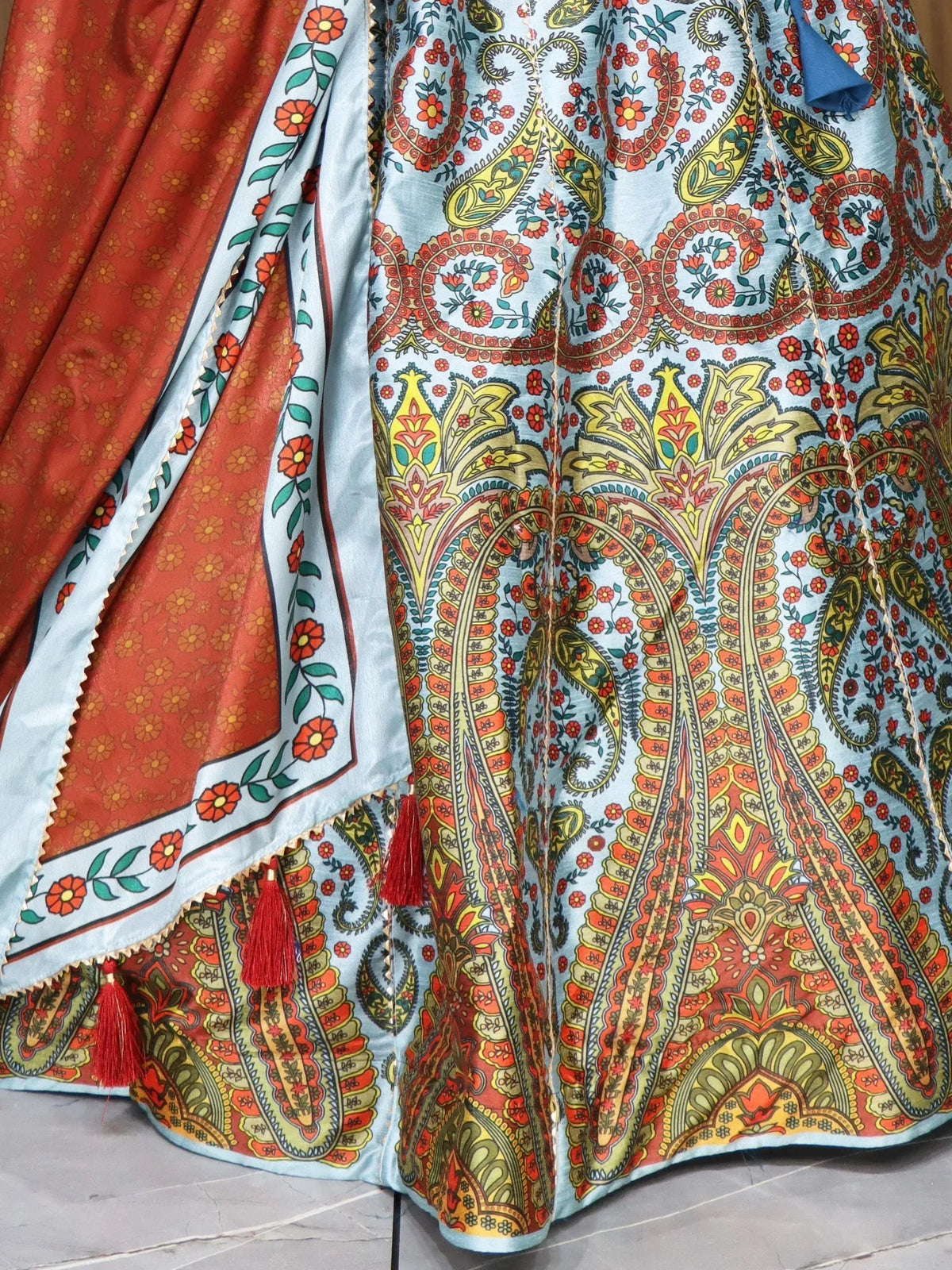 Blue and orange paisley printed lehenga with floral border and red tassels, ethnic Indian wear