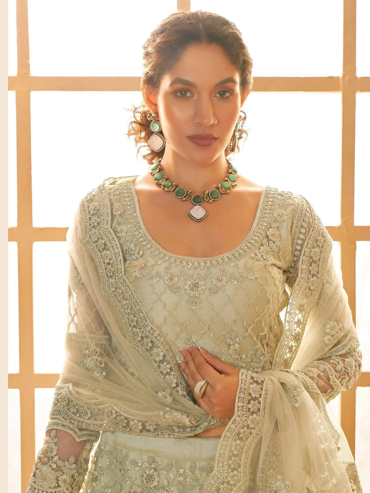 Elegant Indian ethnic wear with intricate embroidery and green stone jewelry, perfect for festive occasions.