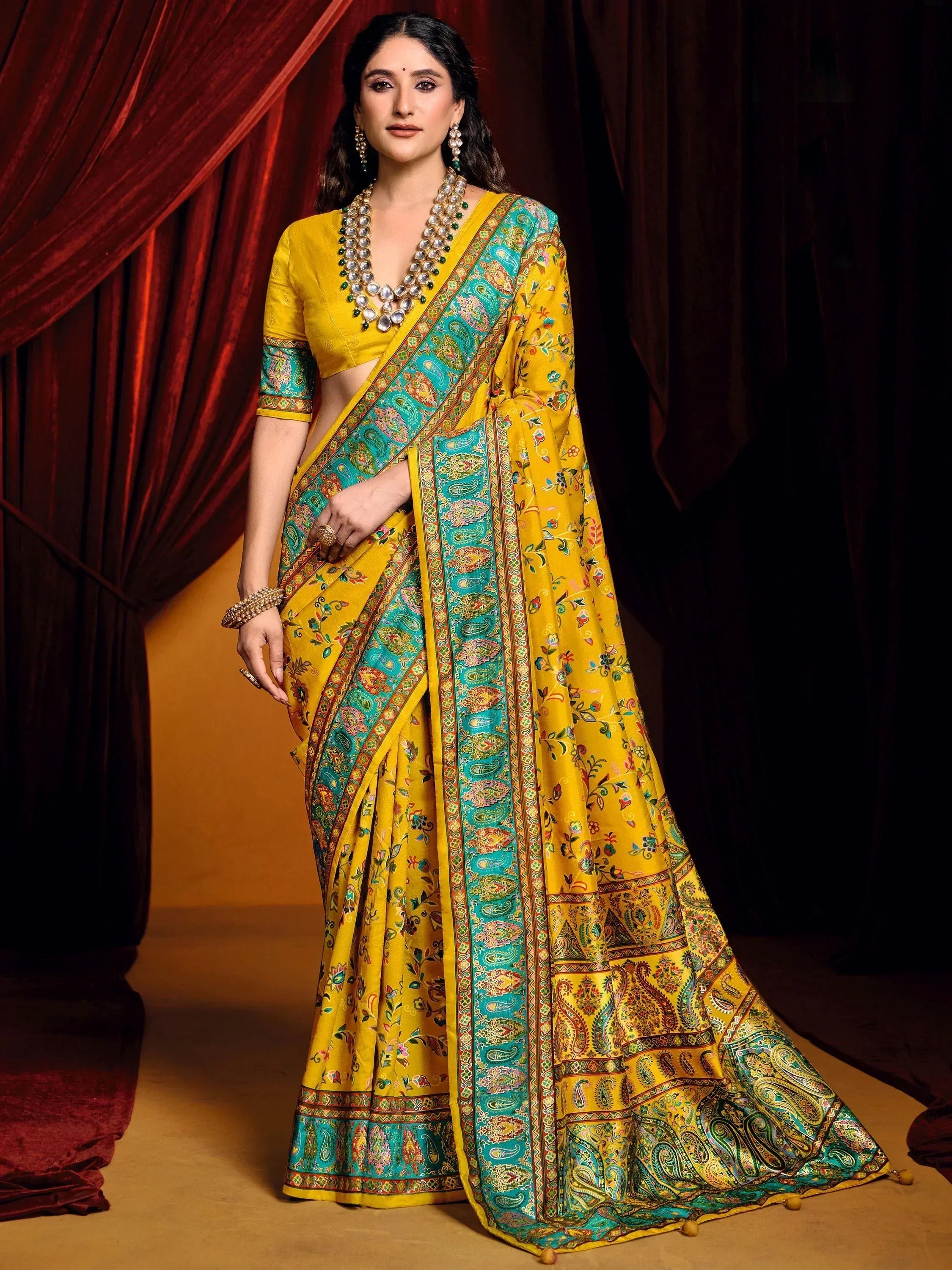Yellow and turquoise printed saree with paisley border, paired with matching blouse and traditional jewelry