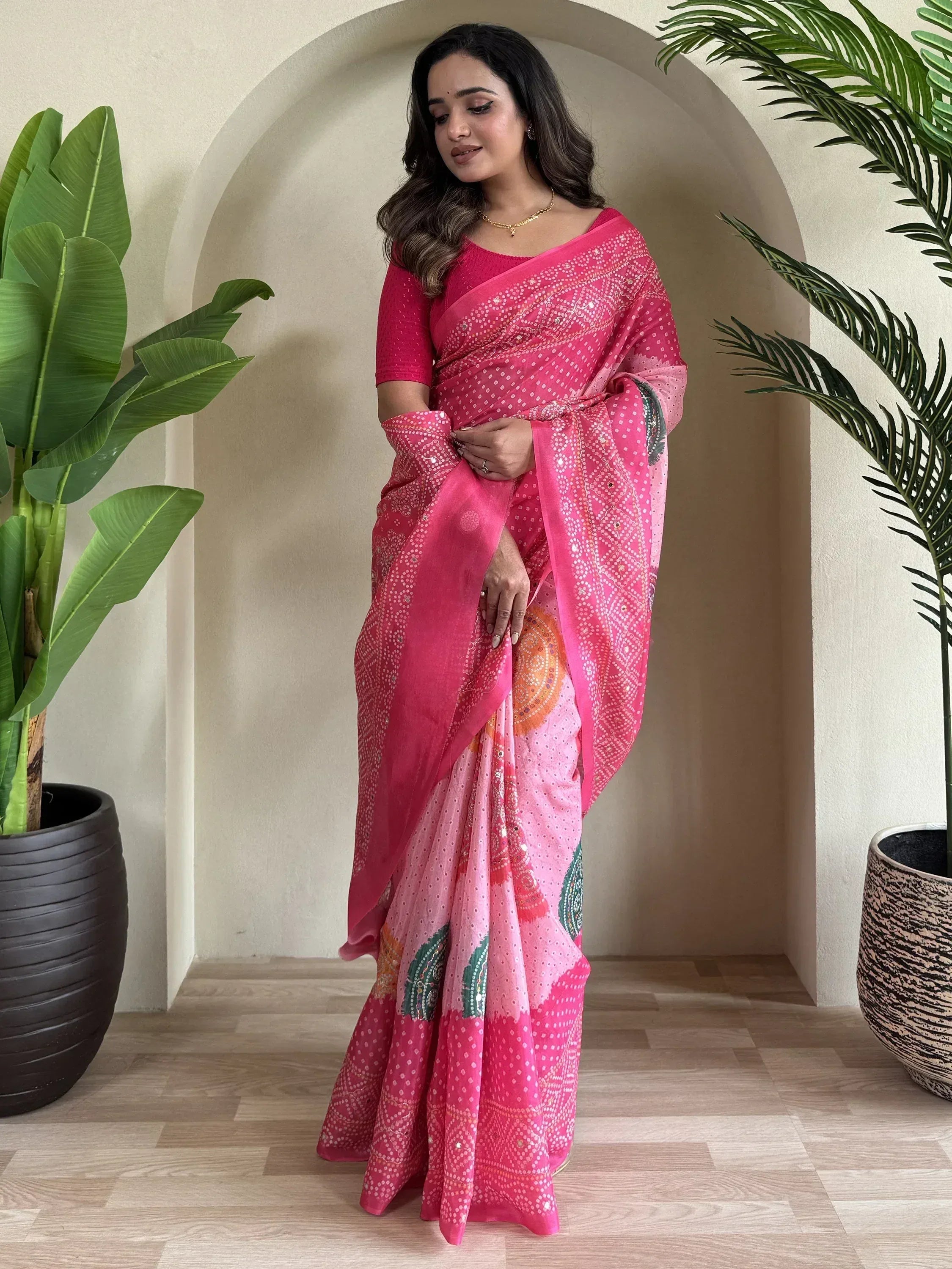 Woman in pink printed saree with mirror work, styled with matching blouse, perfect for ethnic occasions.