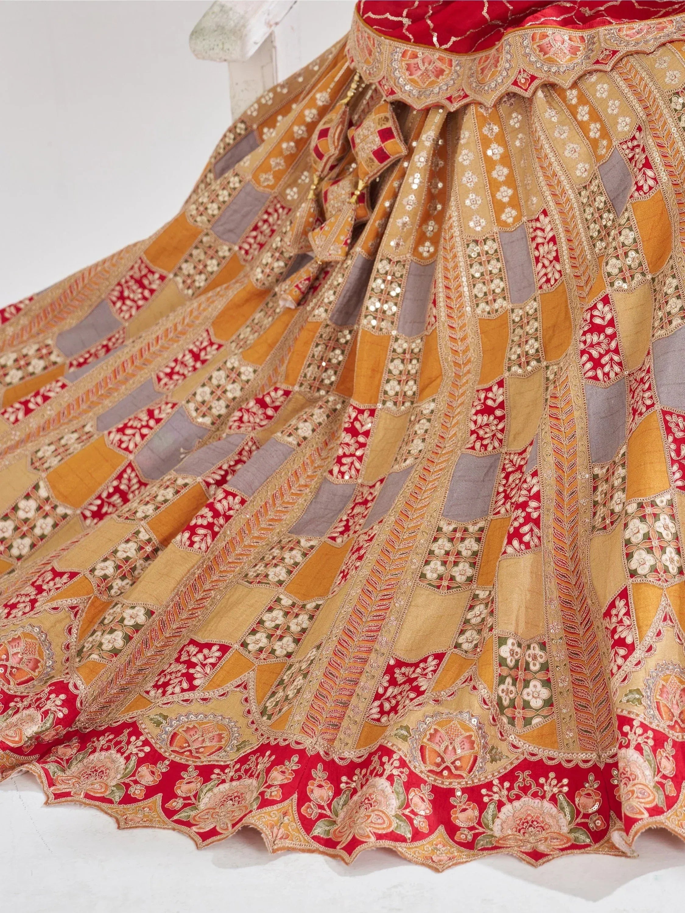 Designer lehenga choli with intricate floral embroidery and patchwork in red, gold, and grey tones