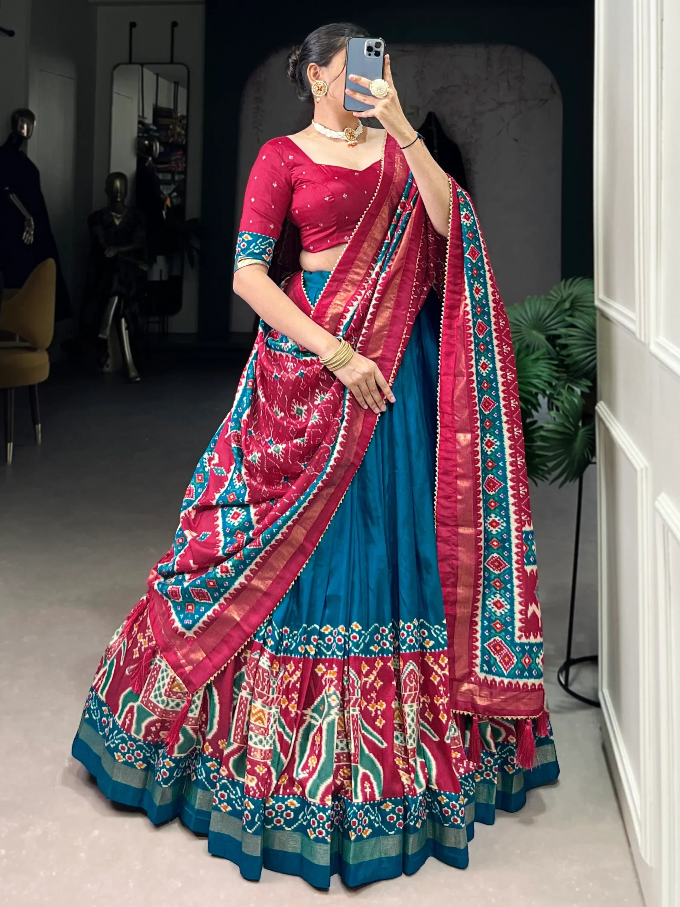 Woman in vibrant red and teal ethnic lehenga choli with intricate patterns, taking mirror selfie