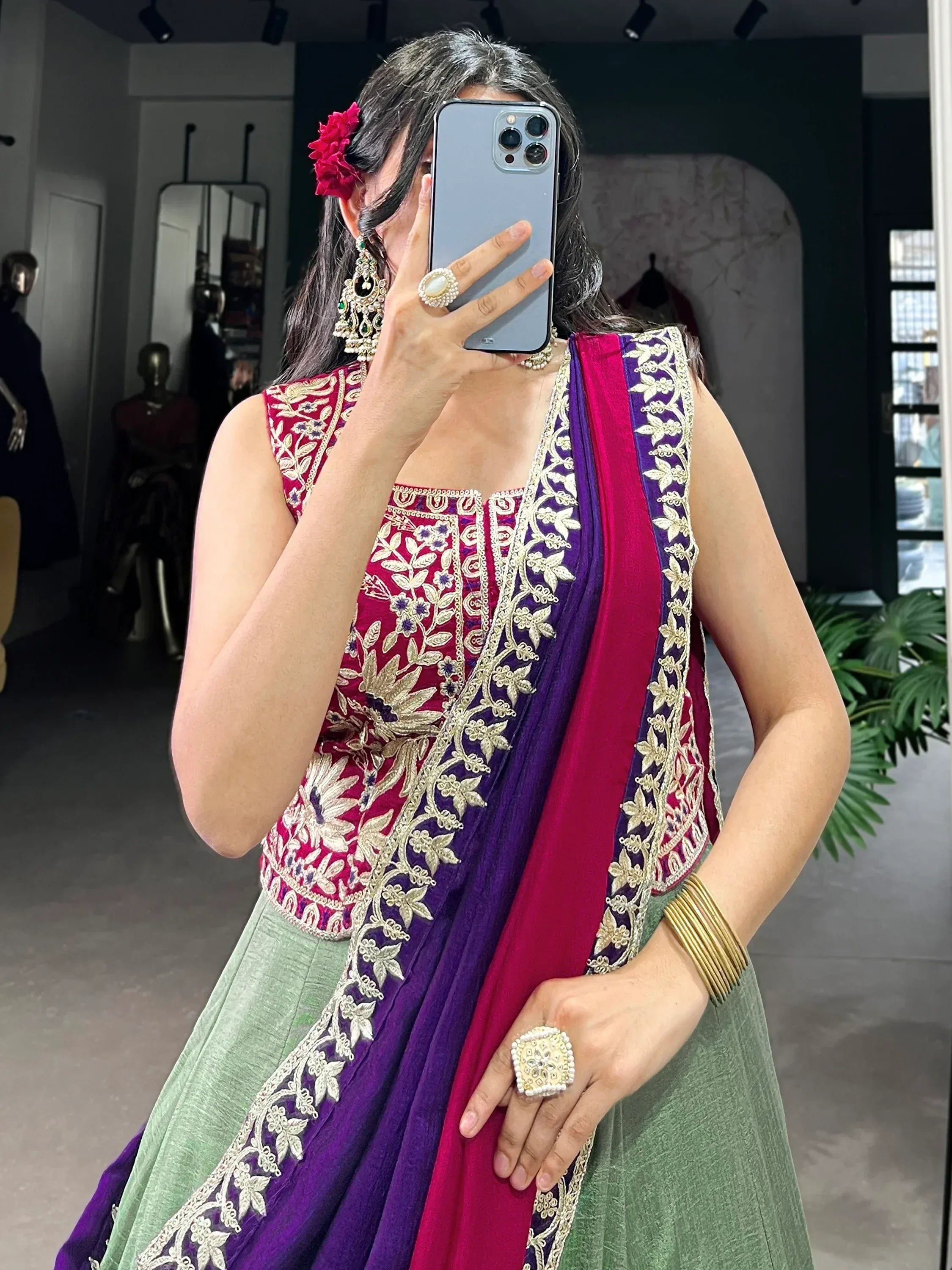 Woman in embroidered magenta and green Indian ethnic wear with gold detailing, taking mirror selfie