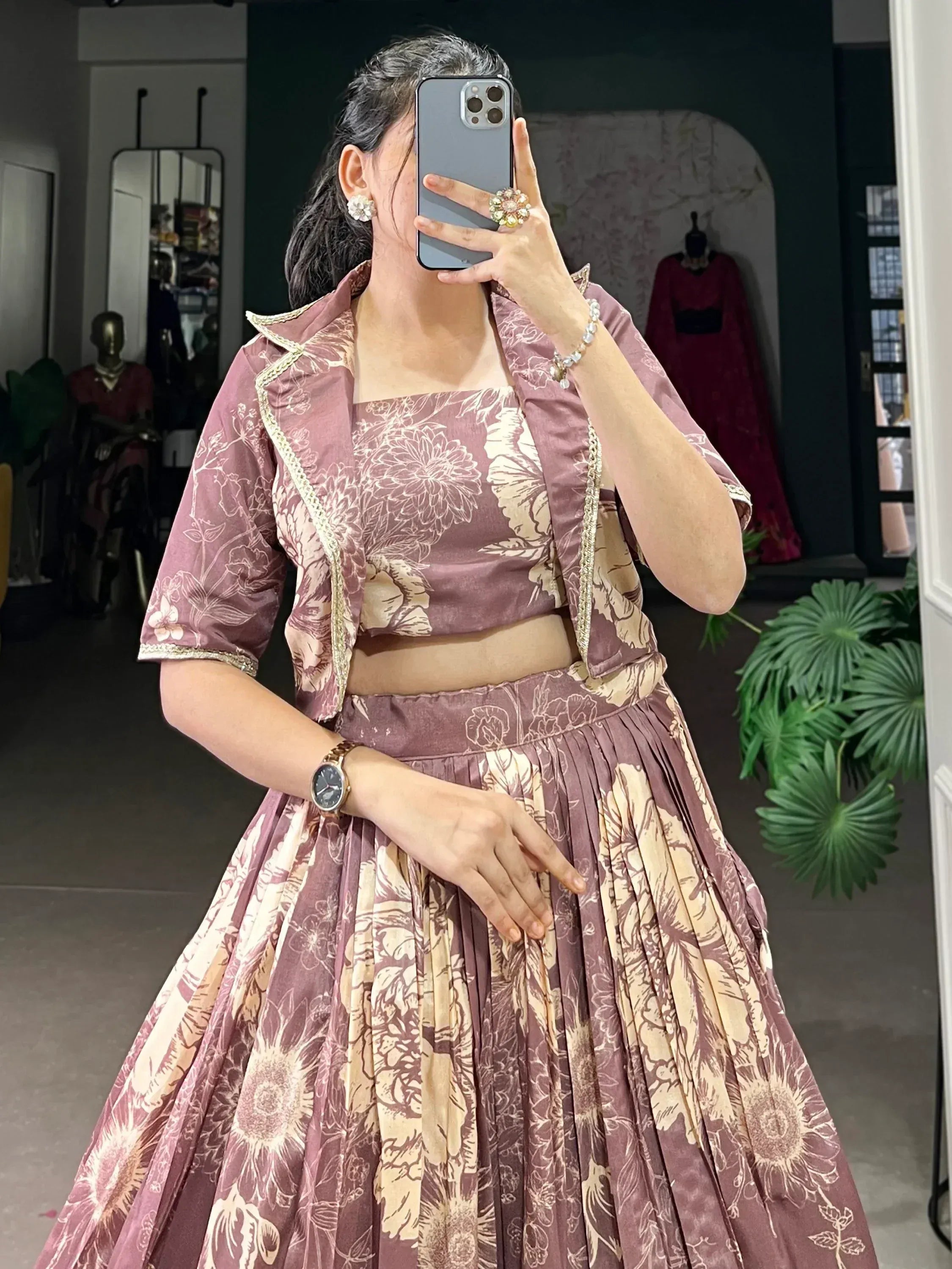 Woman in mauve floral lehenga choli with gold trim, taking mirror selfie in boutique