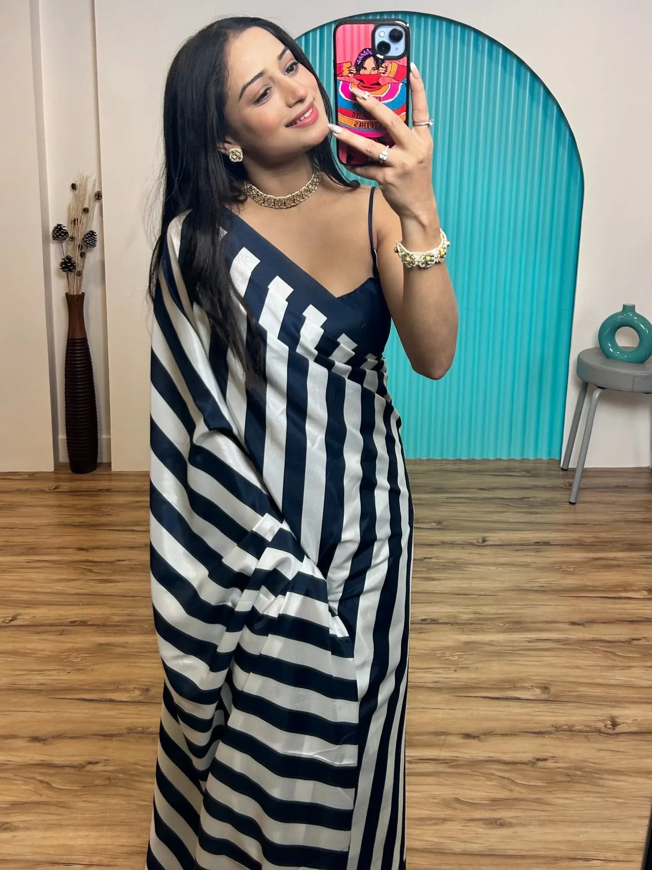 Woman in black and white striped saree with gold jewelry, taking mirror selfie