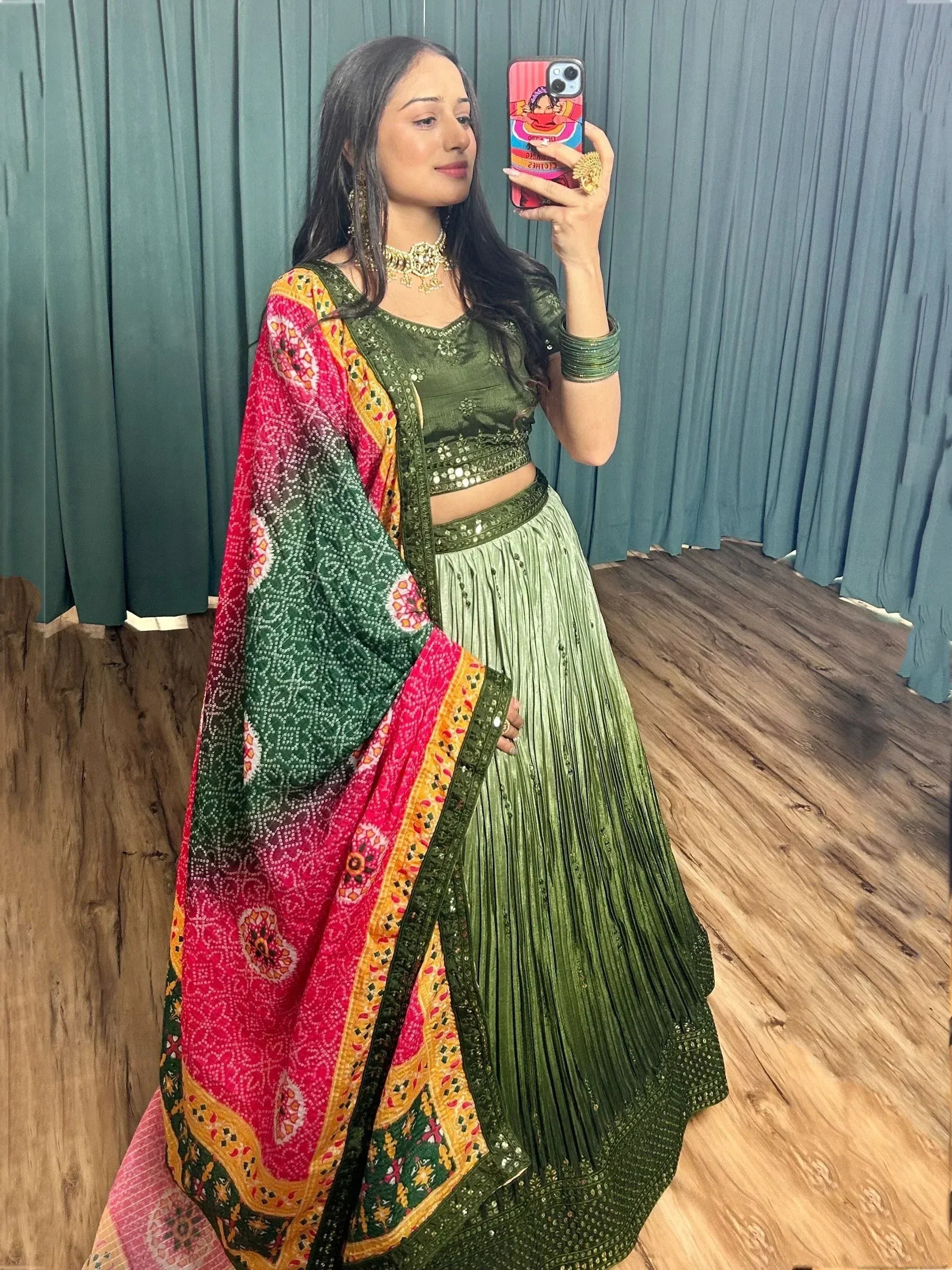Woman in green sequined lehenga choli with colorful bandhani dupatta, taking mirror selfie