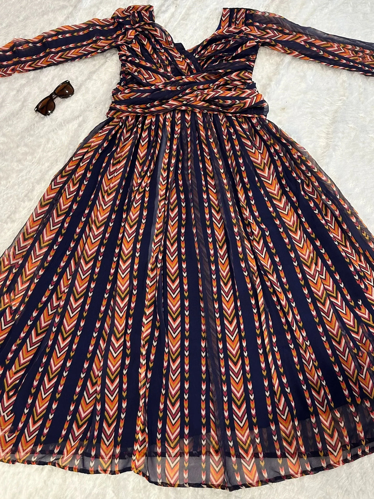 Ethnic printed gown with pleated skirt, long sleeves, and tie waist, paired with sunglasses on white background