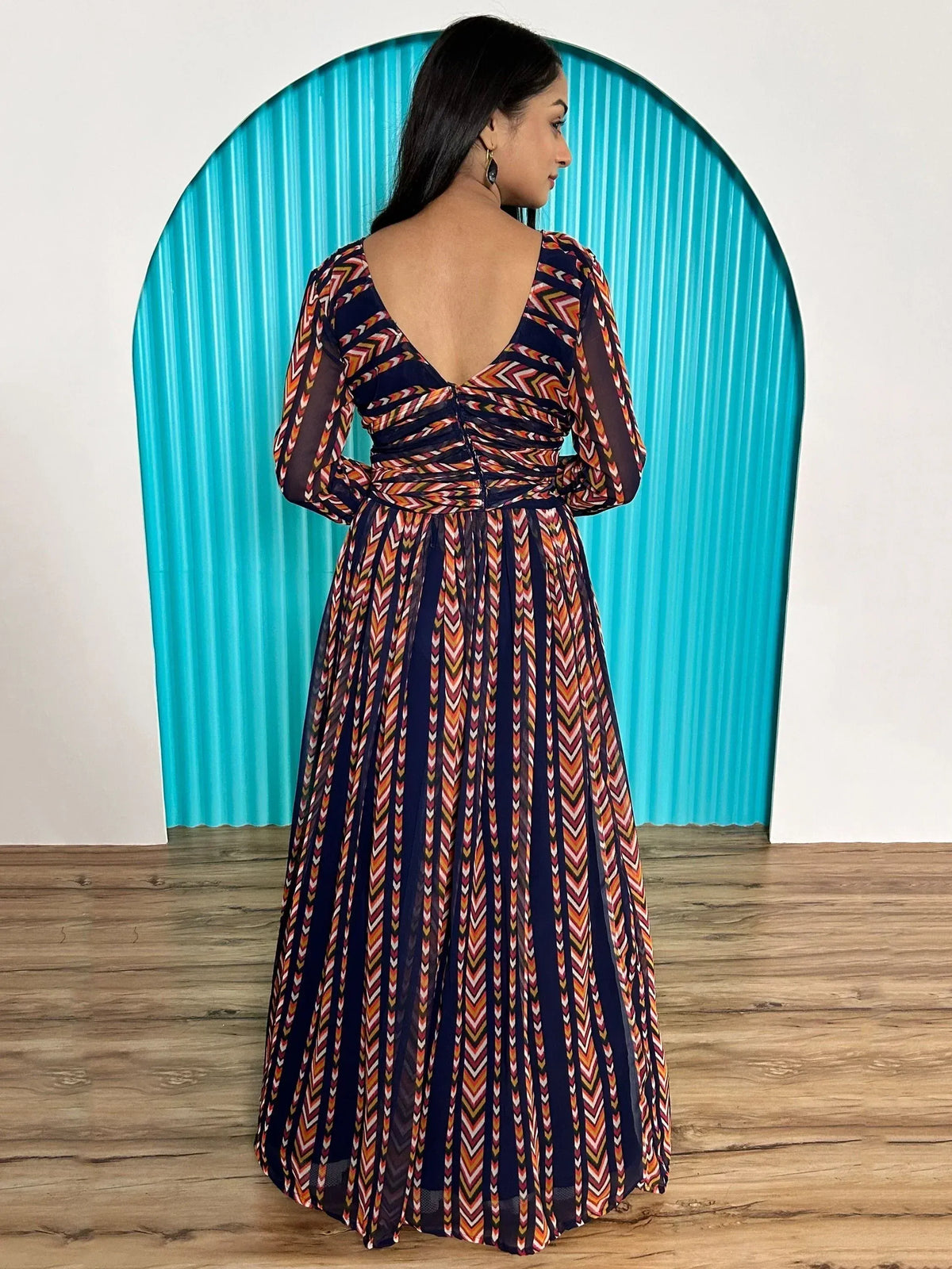 Woman in ethnic printed gown with backless design, long sleeves, and pleated skirt, perfect for festive occasions.