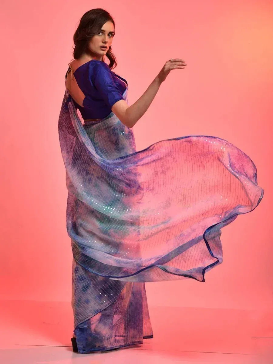 Woman in flowing blue and pink tie-dye saree with sequins, styled with blue blouse for ethnic wear