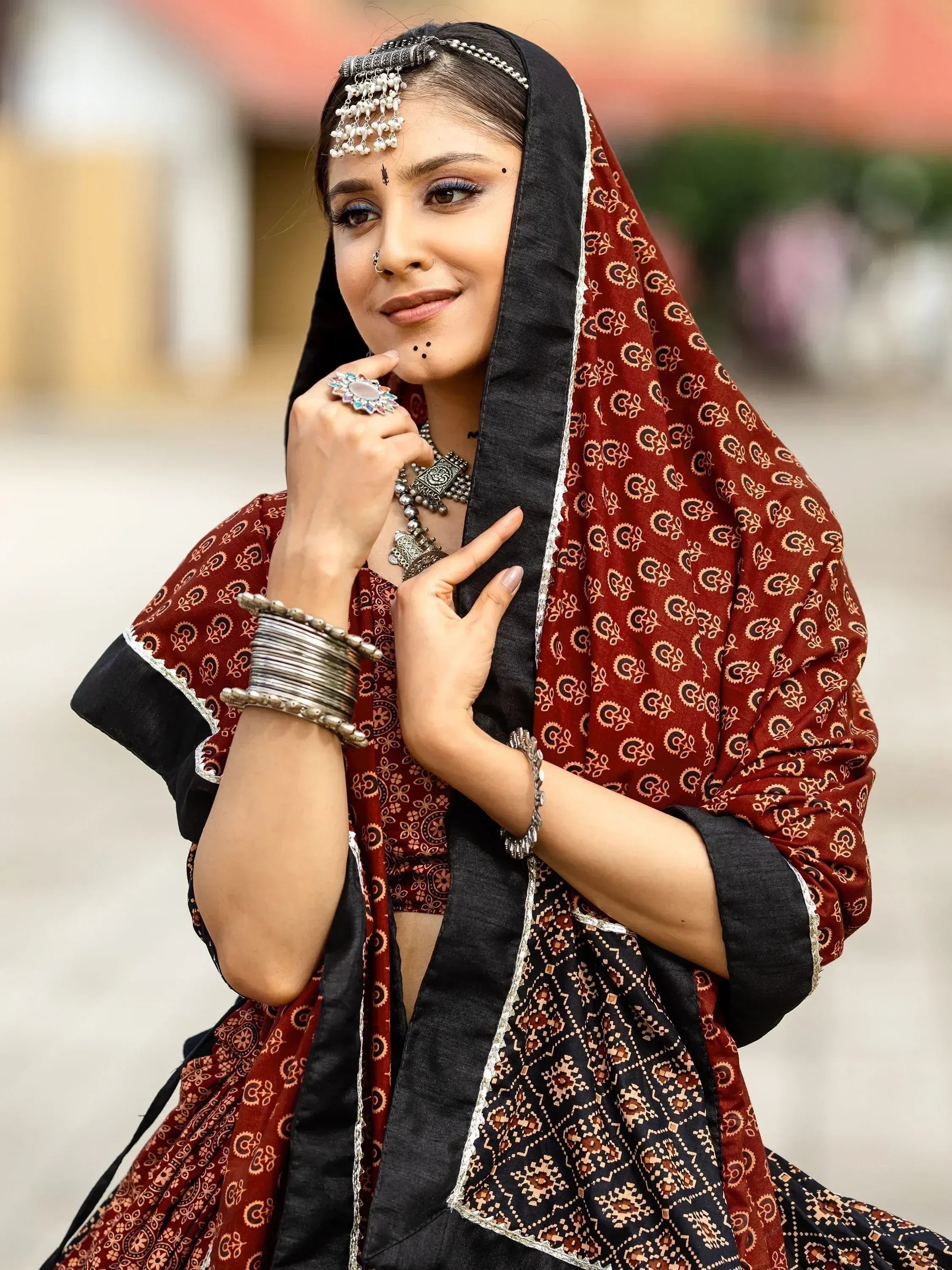Woman in maroon and black printed ethnic lehenga choli with traditional jewelry and headpiece