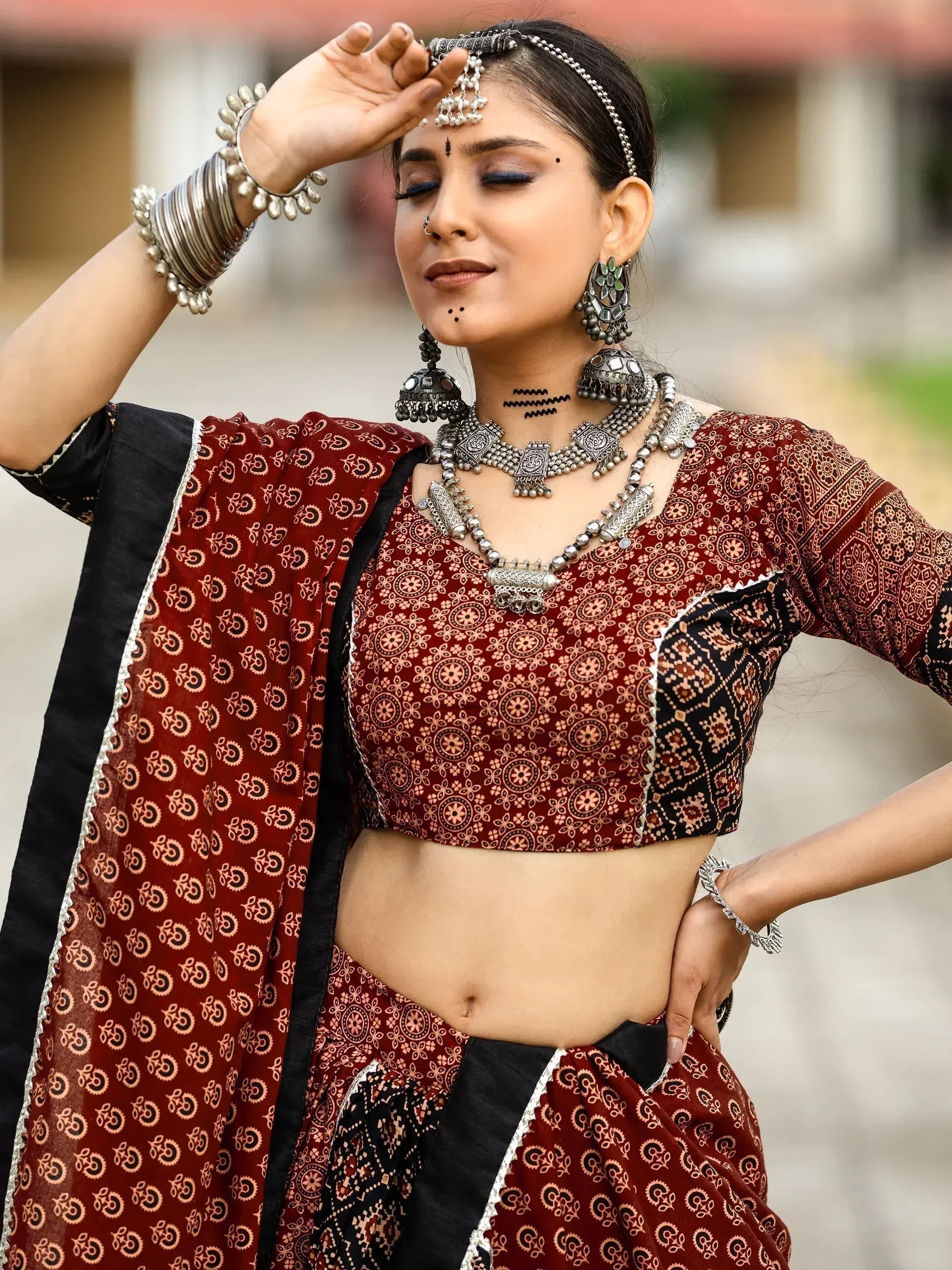 Woman in maroon and black printed ethnic lehenga choli with silver jewelry, traditional Indian attire