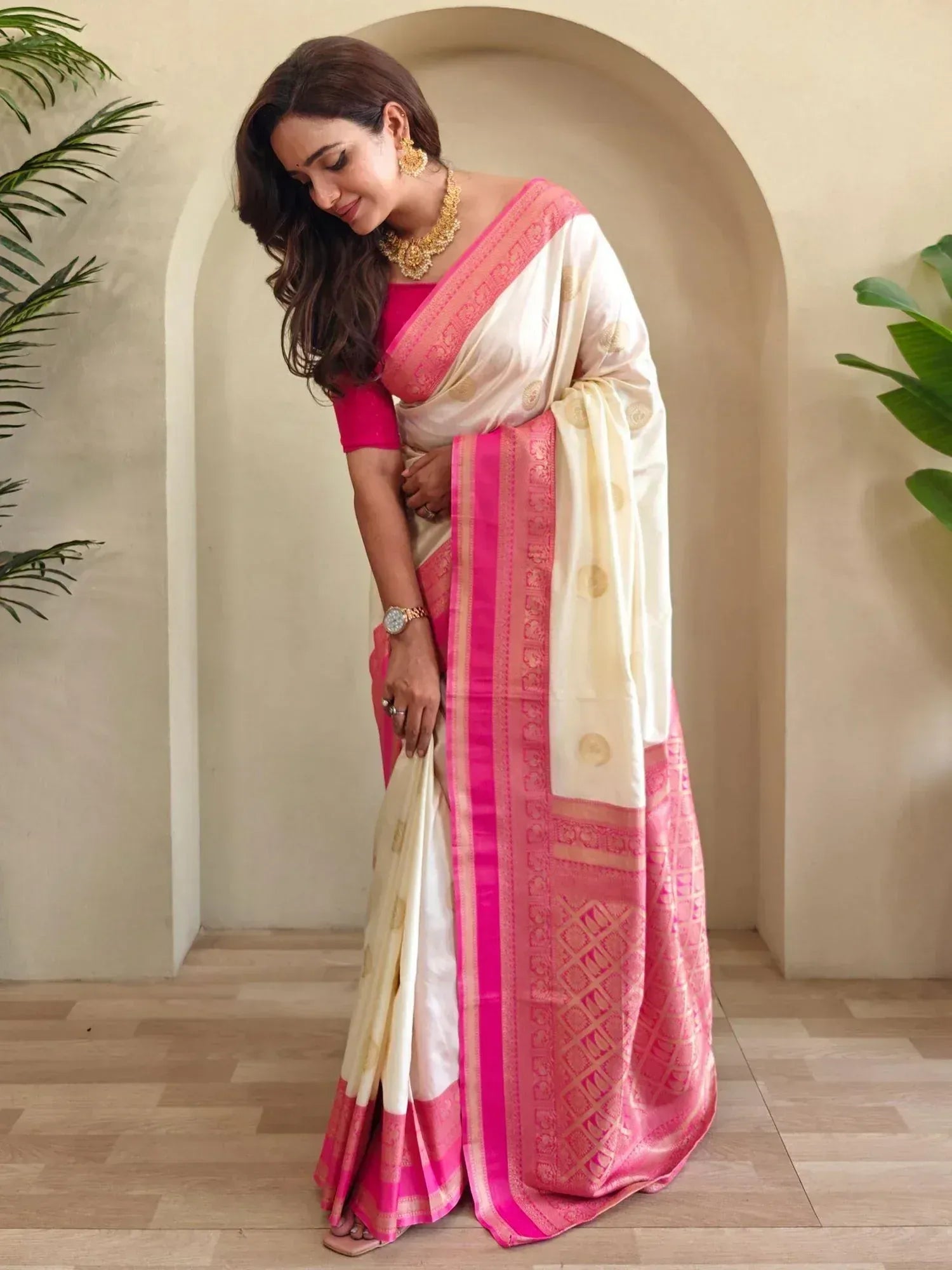 Woman in elegant cream and pink designer saree with gold embroidery, styled with traditional jewelry