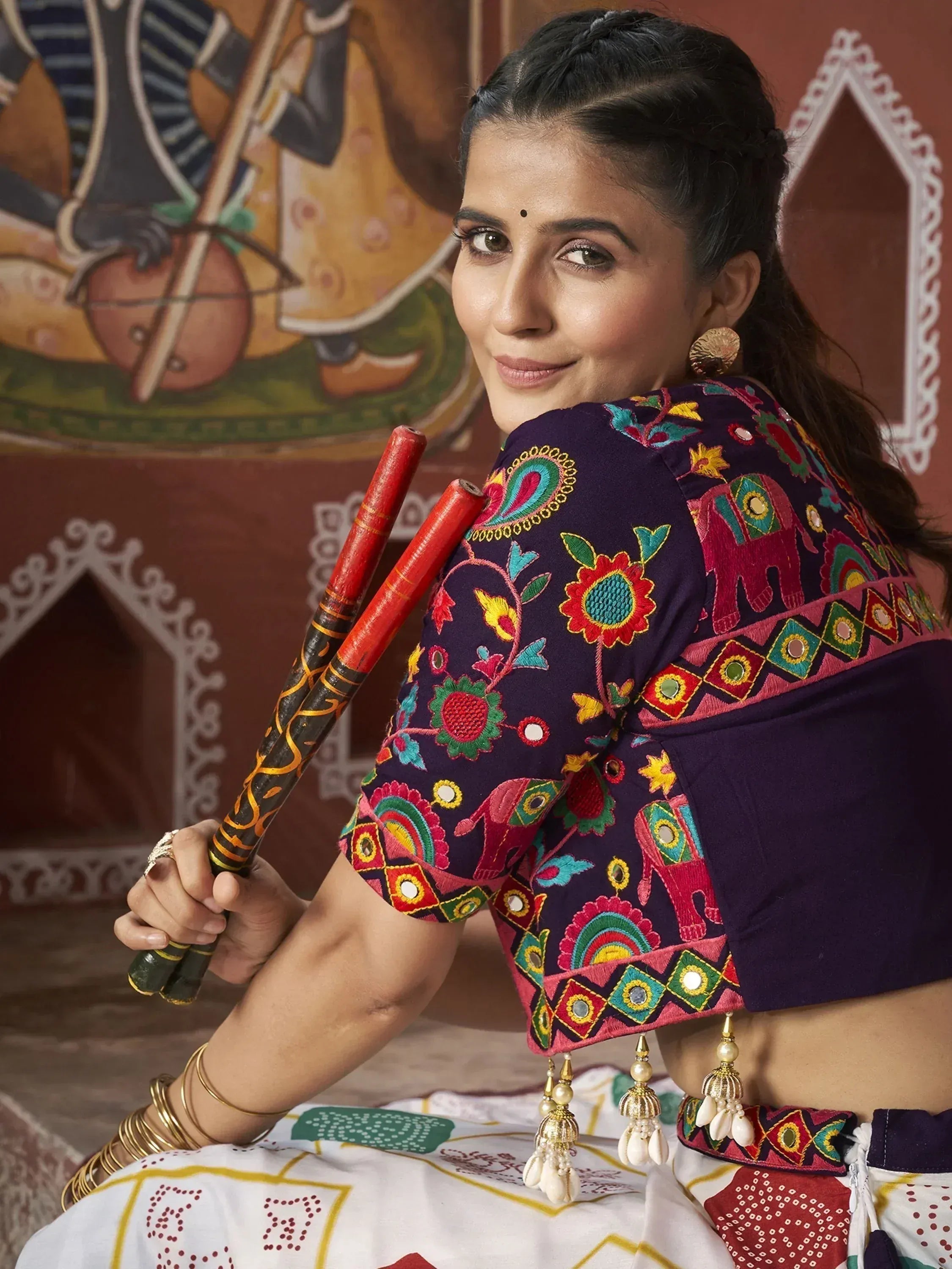 Woman in vibrant embroidered Indian ethnic wear with mirror work, holding dandiya sticks, traditional festive attire