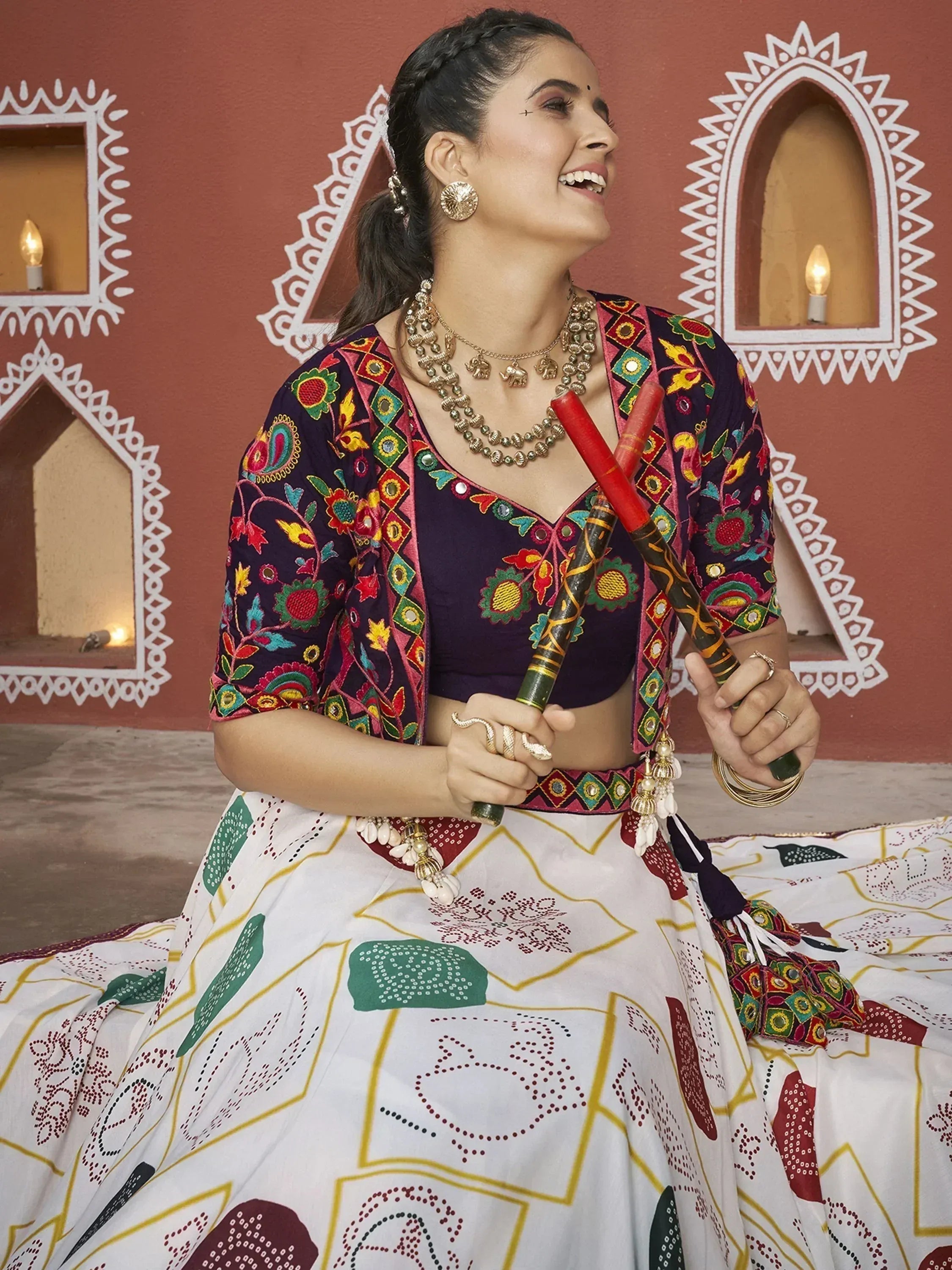 Woman in colorful embroidered lehenga choli with dupatta, holding dandiya sticks, festive Indian ethnic wear