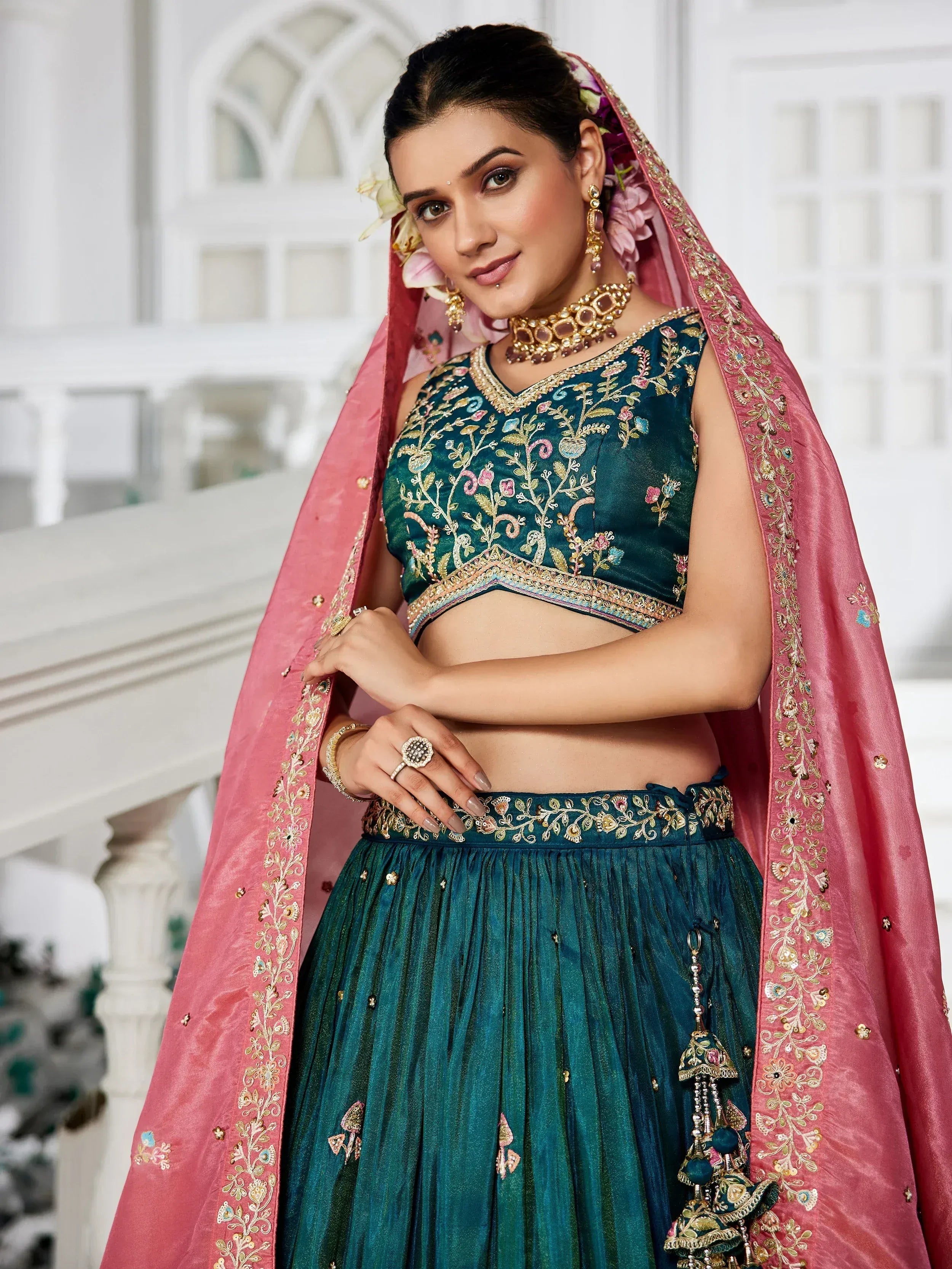 Teal embroidered lehenga choli with pink dupatta, floral motifs, and gold jewelry for Indian ethnic wear