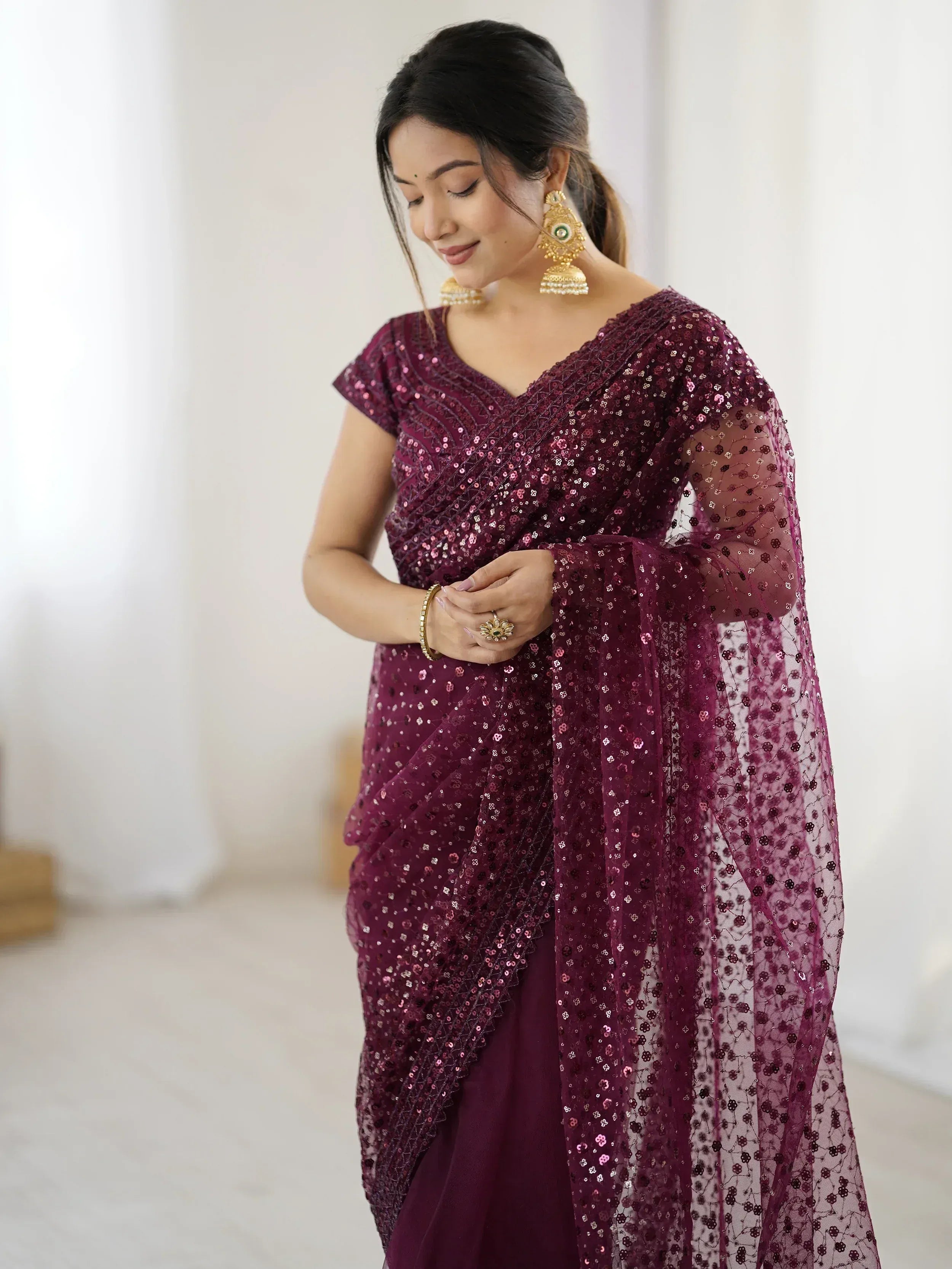 Woman in maroon sequin saree with sheer overlay, gold jewelry, perfect for Indian ethnic occasions