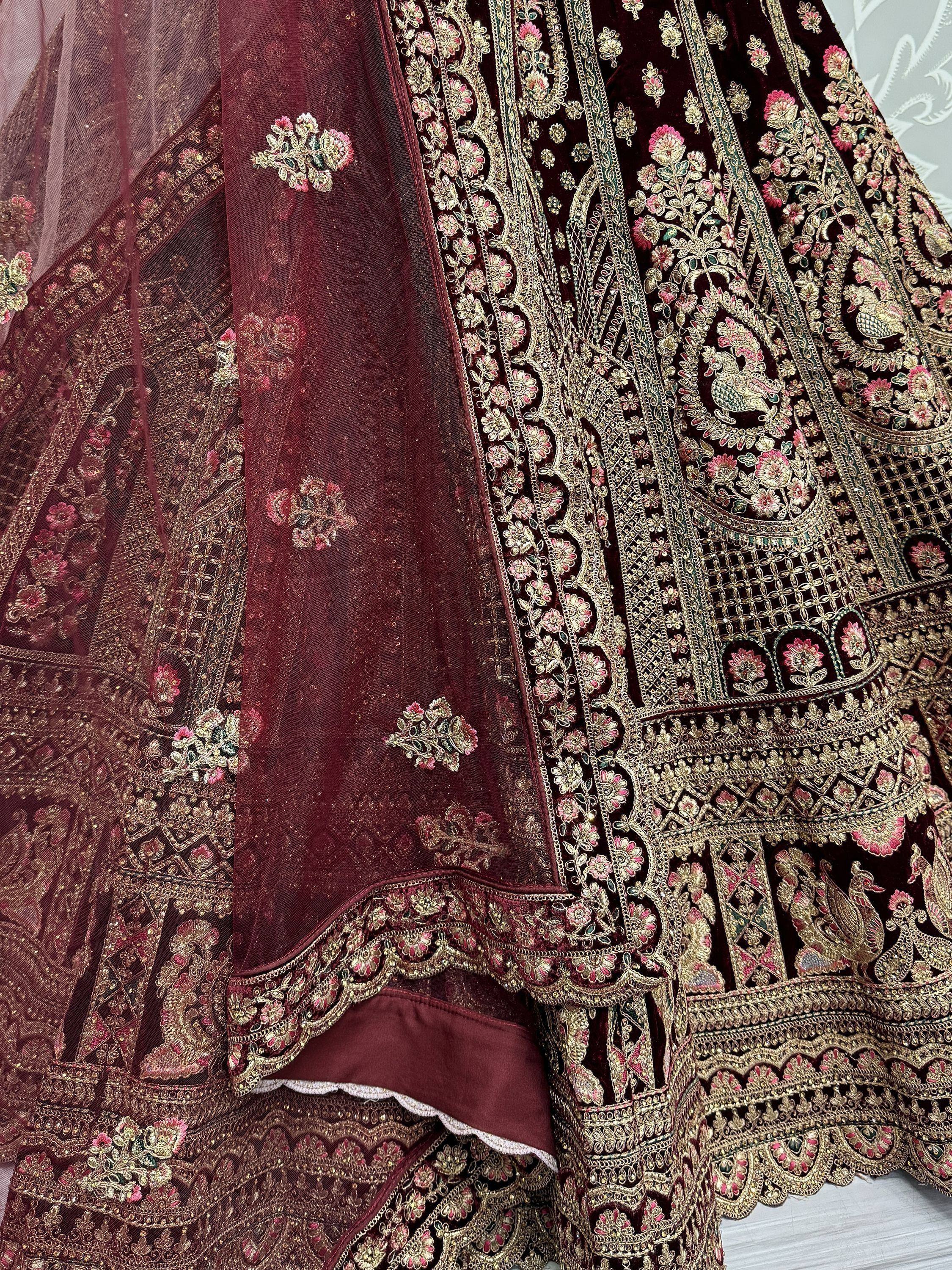 Luxury maroon velvet lehenga choli with intricate gold and pink floral embroidery, perfect for Indian weddings.