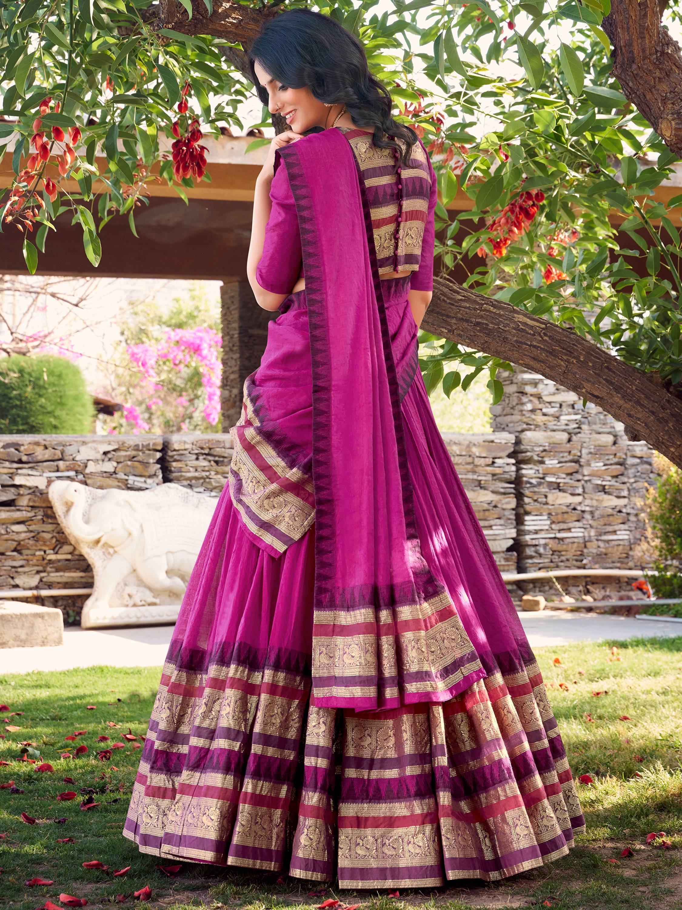 Purple ethnic saree with gold border, worn outdoors under tree with floral backdrop