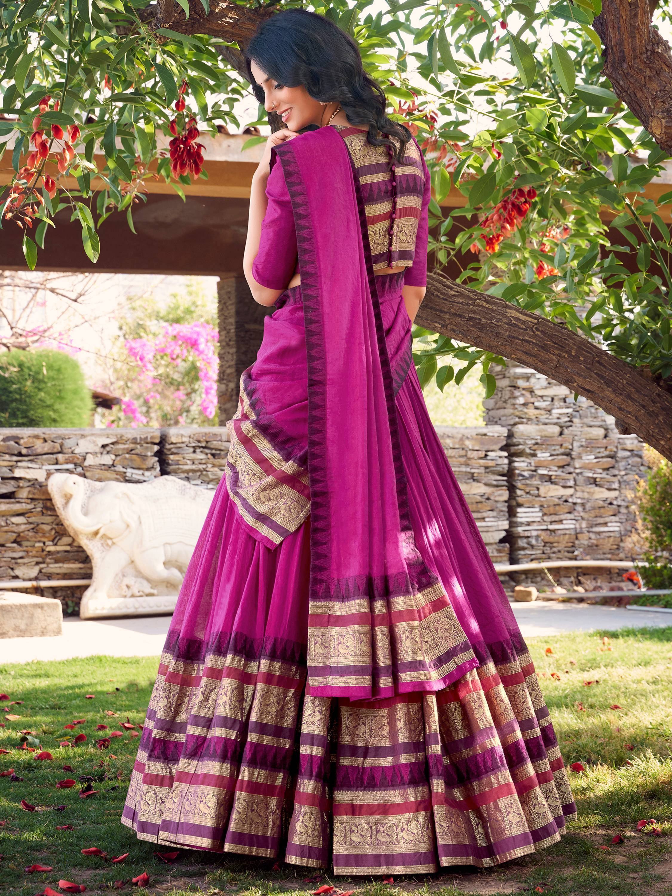 Purple ethnic saree with gold border, worn outdoors under tree with floral backdrop