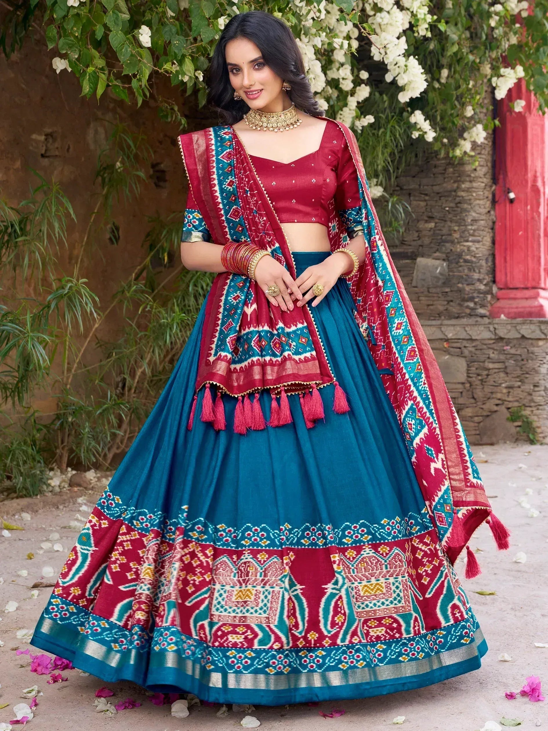 Woman in vibrant red and teal designer lehenga choli with ethnic print, perfect for Indian weddings and festive occasions.