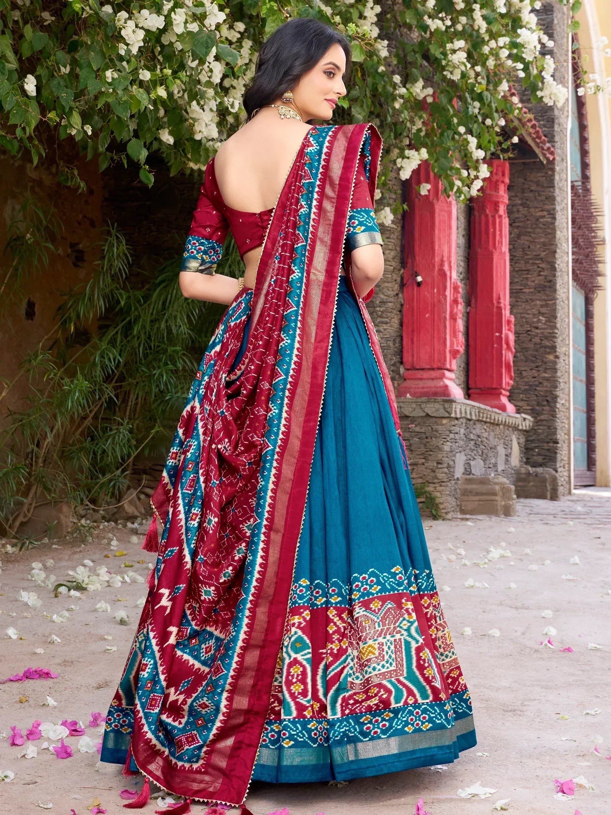 Woman in maroon and teal designer lehenga choli with intricate patterns, perfect for ethnic occasions.