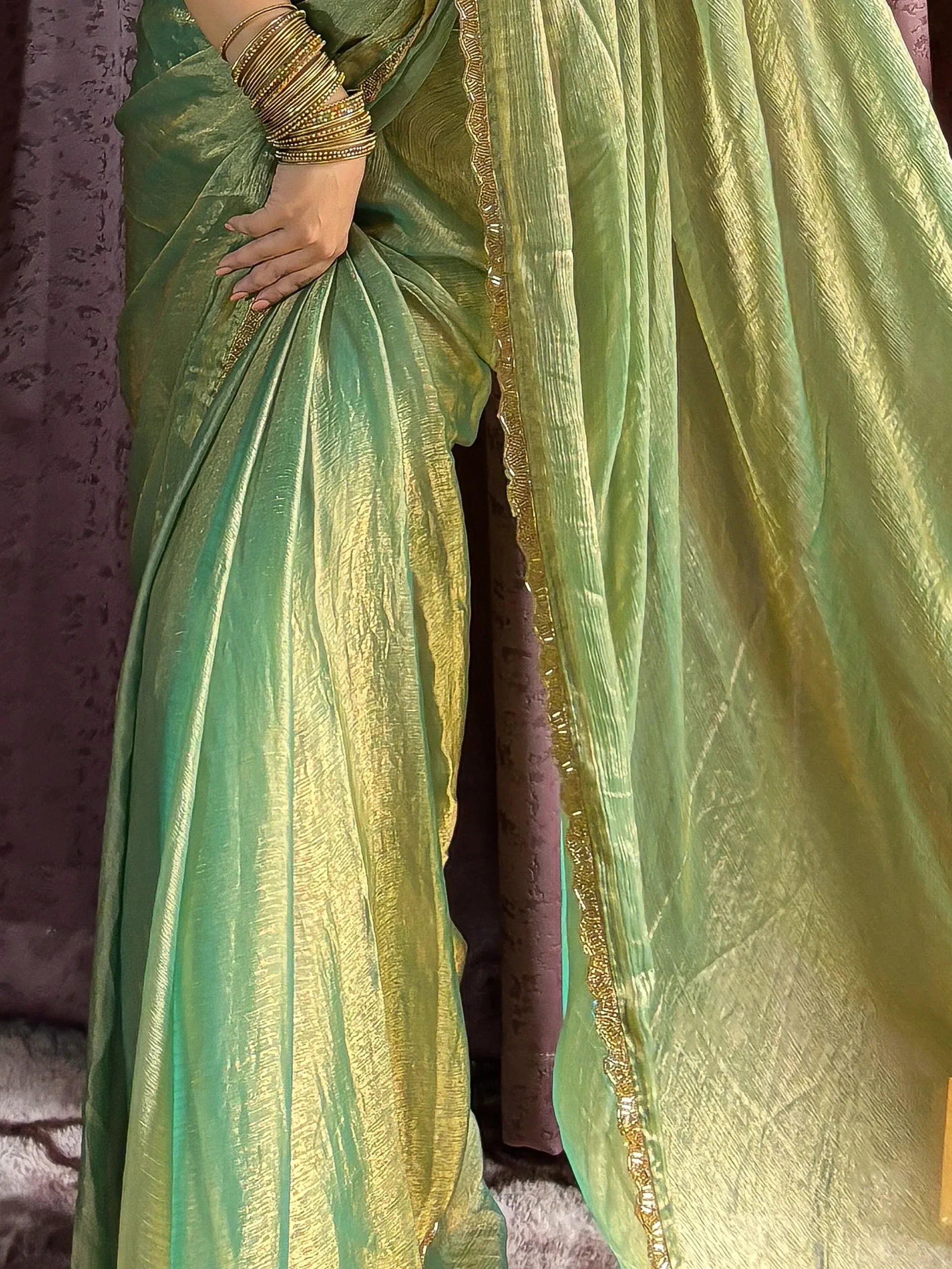 Green and gold shimmer saree with intricate border, styled with traditional bangles for ethnic wear.