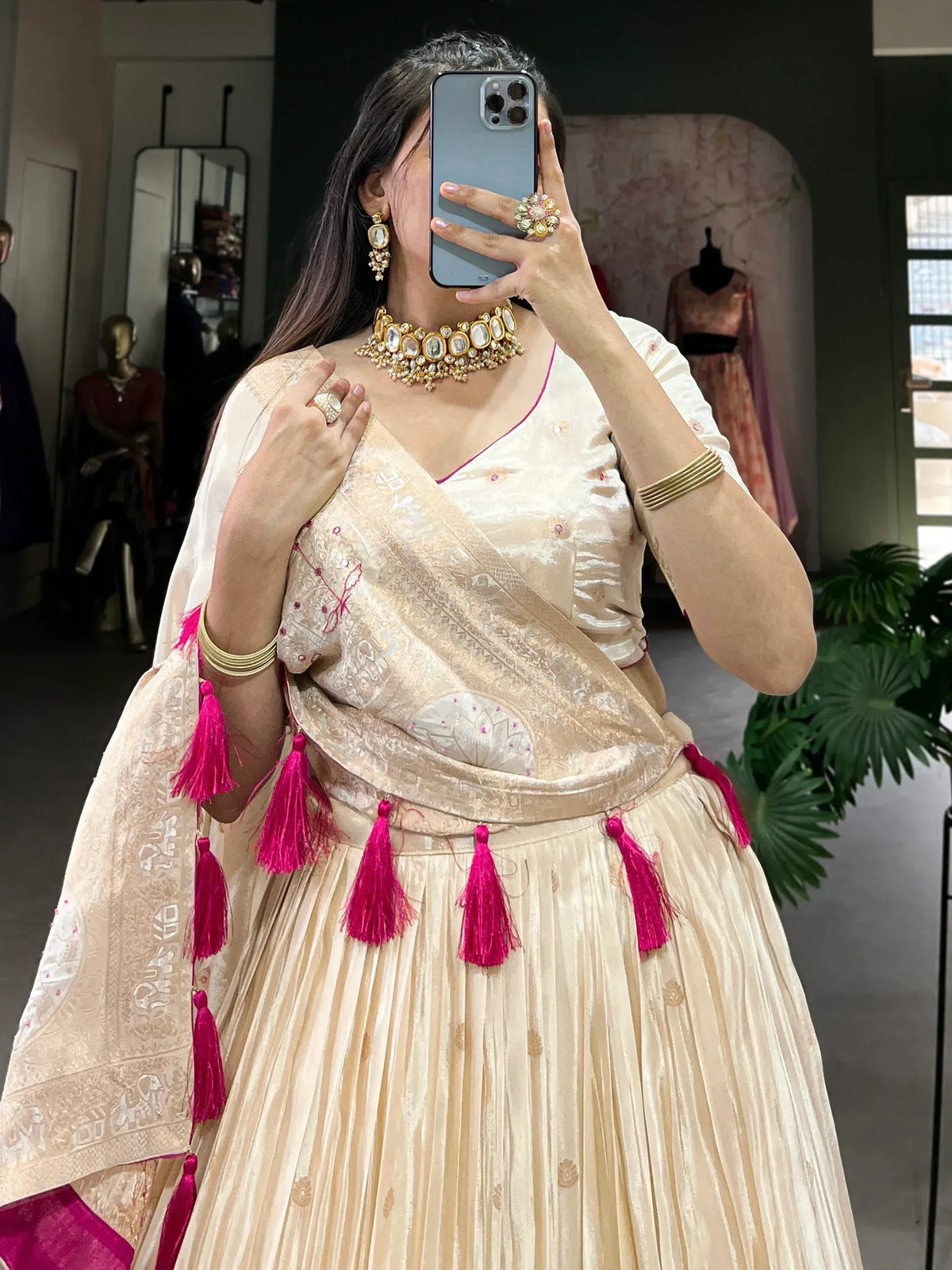 Cream designer lehenga choli with pink tassels and gold jewelry, perfect for Indian ethnic wear