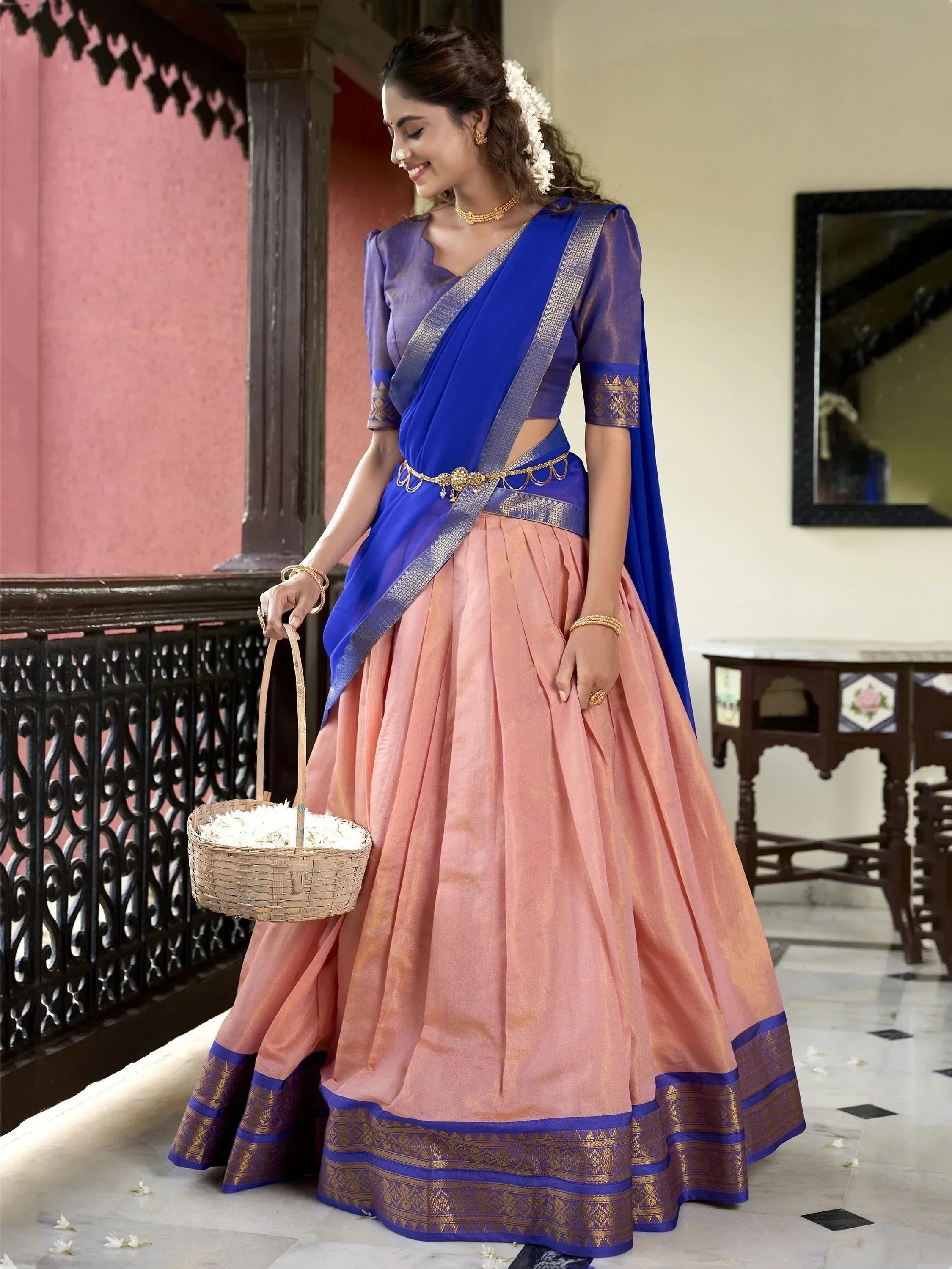 Woman in blue and peach designer lehenga choli with gold border, holding flower basket