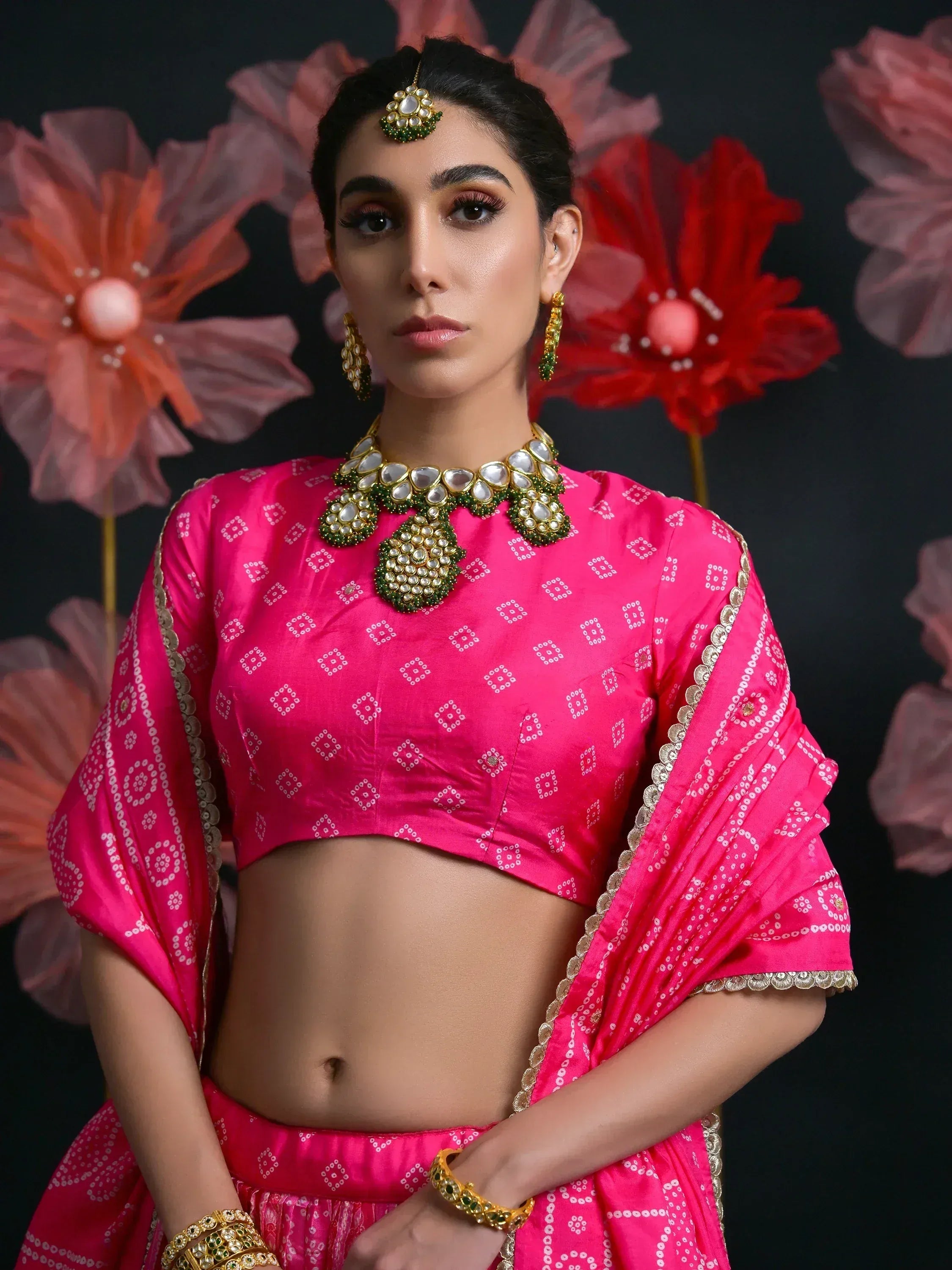 Pink ethnic lehenga choli with white bandhani print, gold trim, and traditional jewelry for Indian weddings