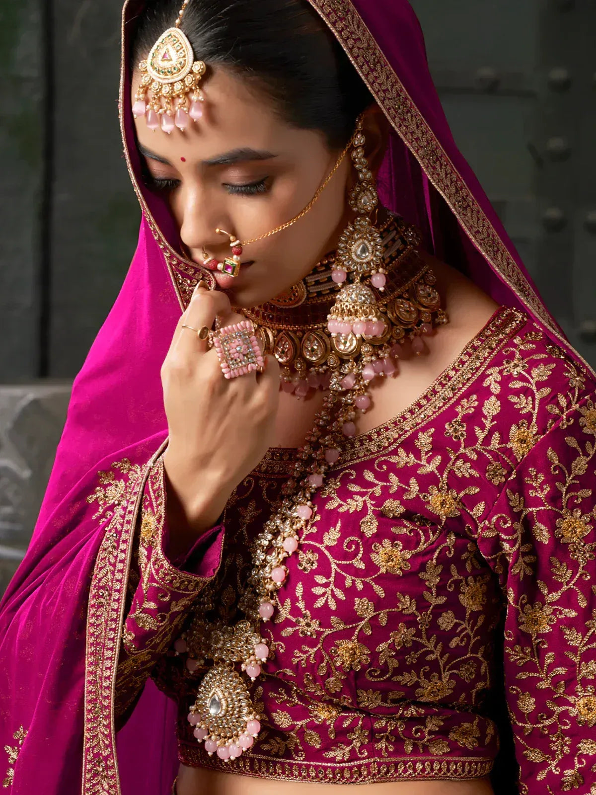 Elegant maroon lehenga choli with gold embroidery, pink beads, and traditional Indian bridal jewelry