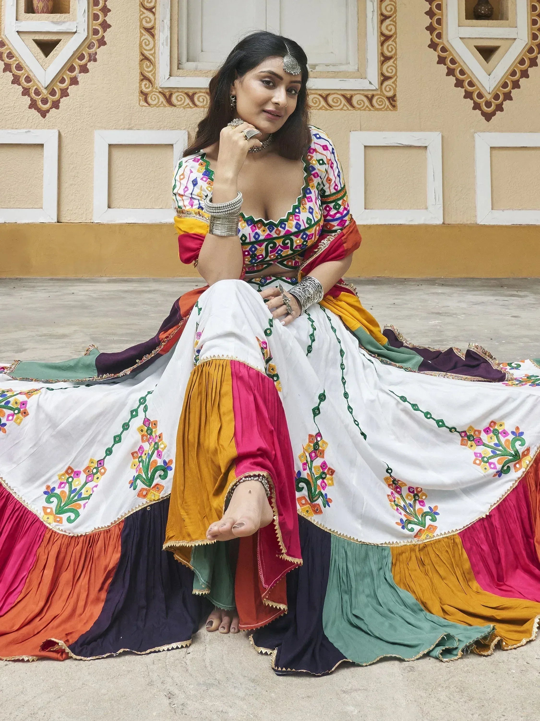 Woman in colorful embroidered Indian ethnic wear with mirror work, sitting against traditional wall
