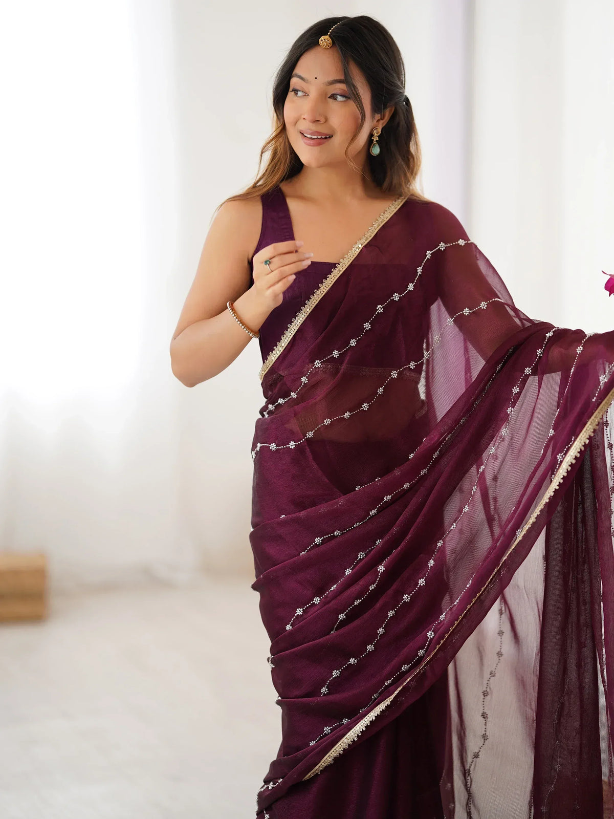 Woman in elegant maroon saree with gold trim and floral embroidery, styled with traditional jewelry for ethnic wear.