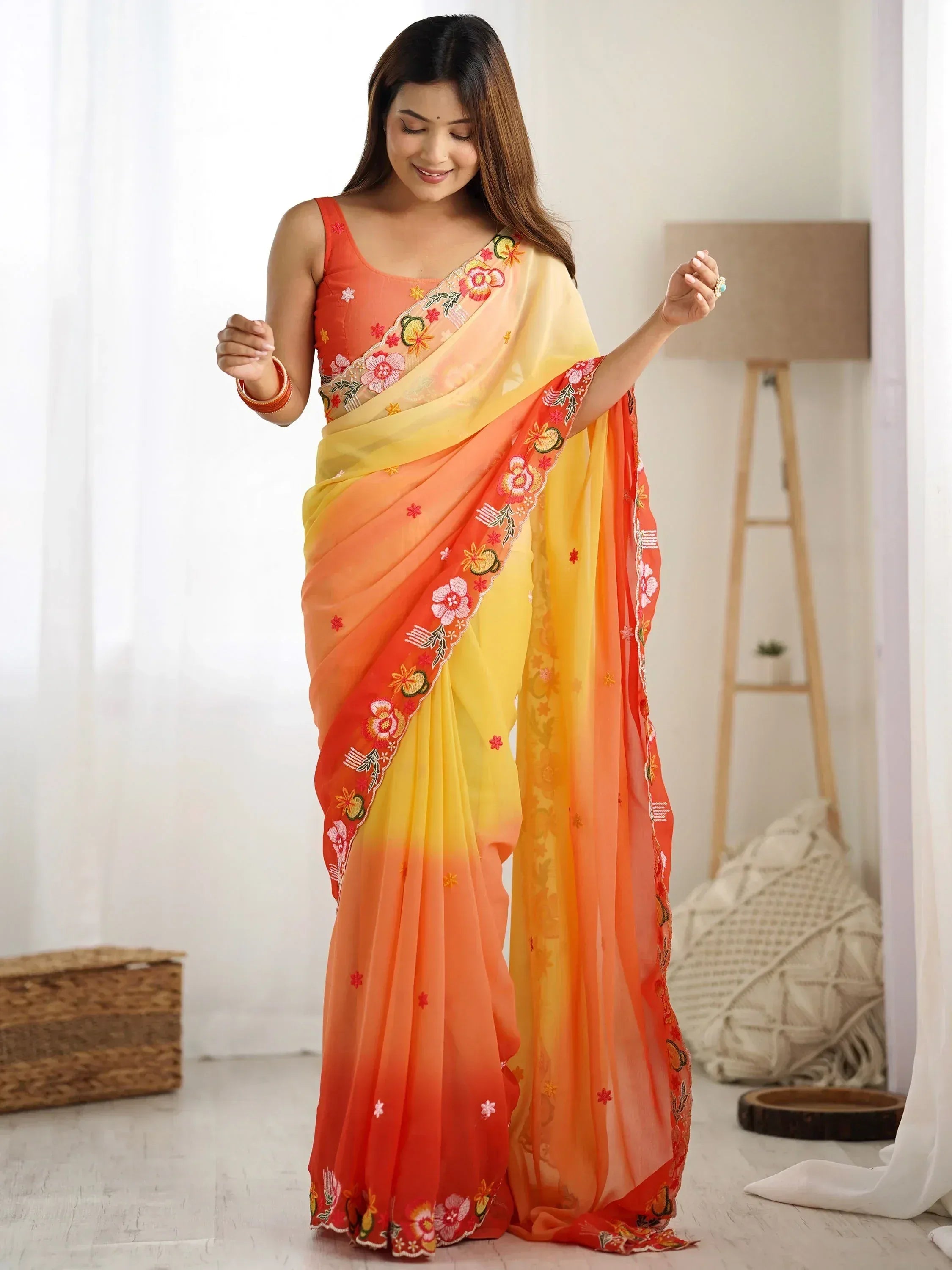 Woman in vibrant orange-yellow ombre saree with floral embroidery, perfect for Indian ethnic occasions