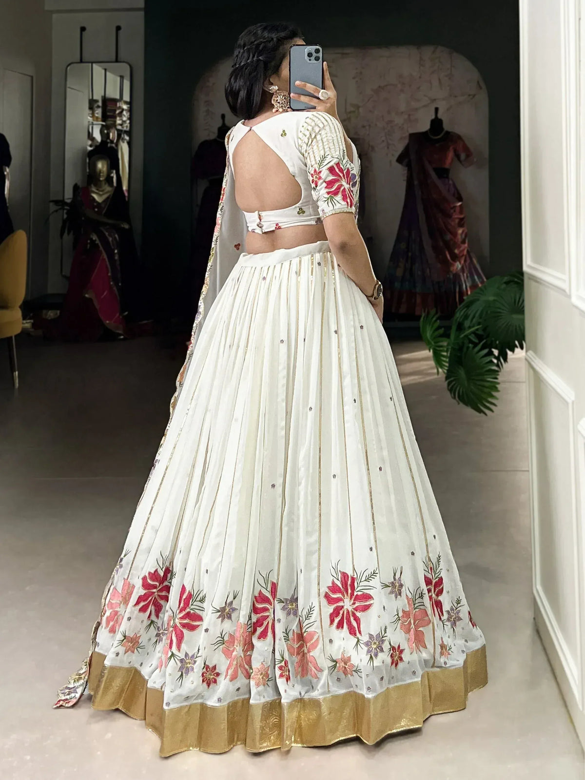 White floral embroidered lehenga choli with gold trim, back view in boutique setting