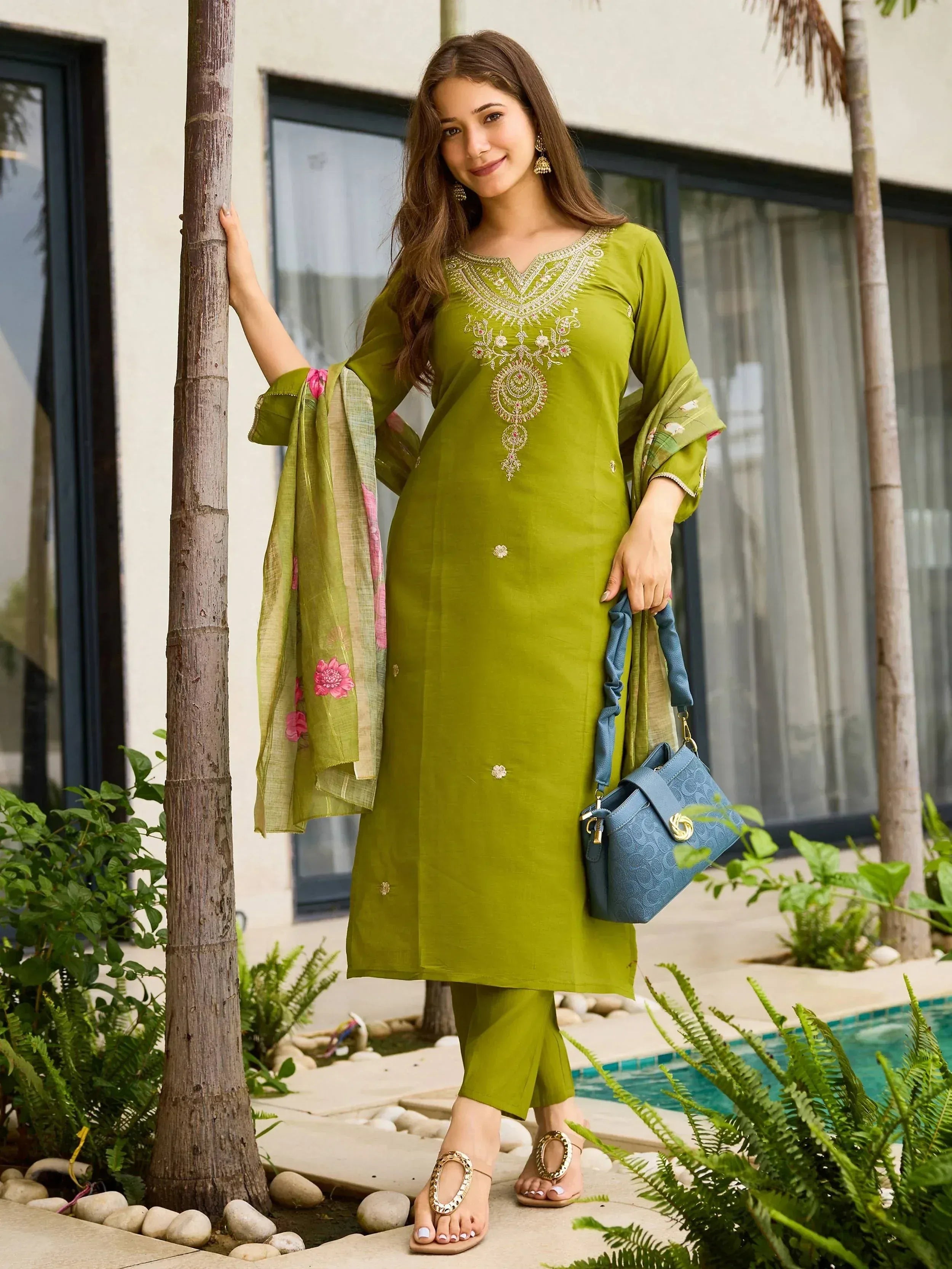 Olive green embroidered kurta with matching pants and floral dupatta, styled with blue handbag near poolside
