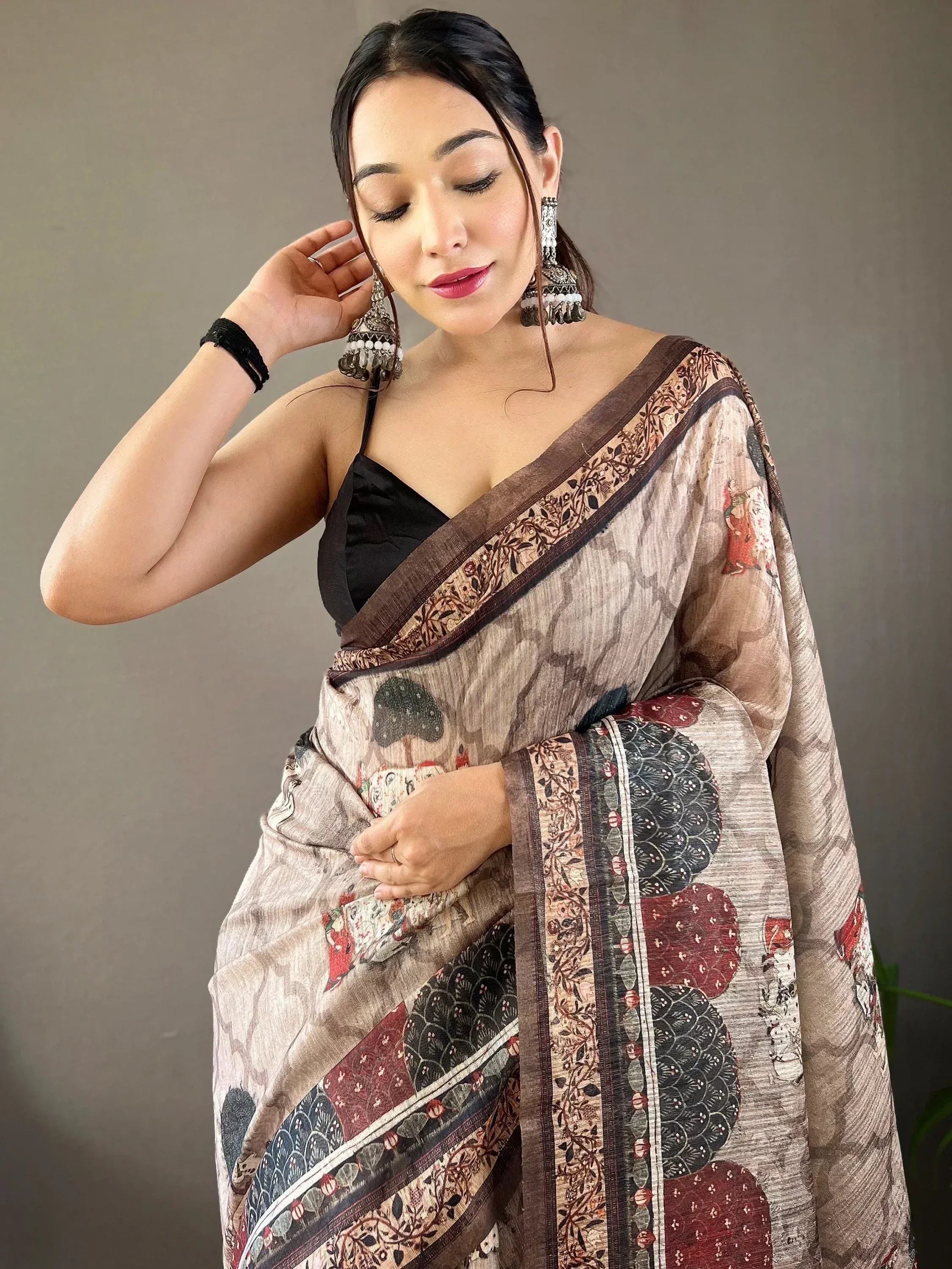Woman in elegant printed saree with floral border, styled with black blouse and jhumka earrings for ethnic wear.