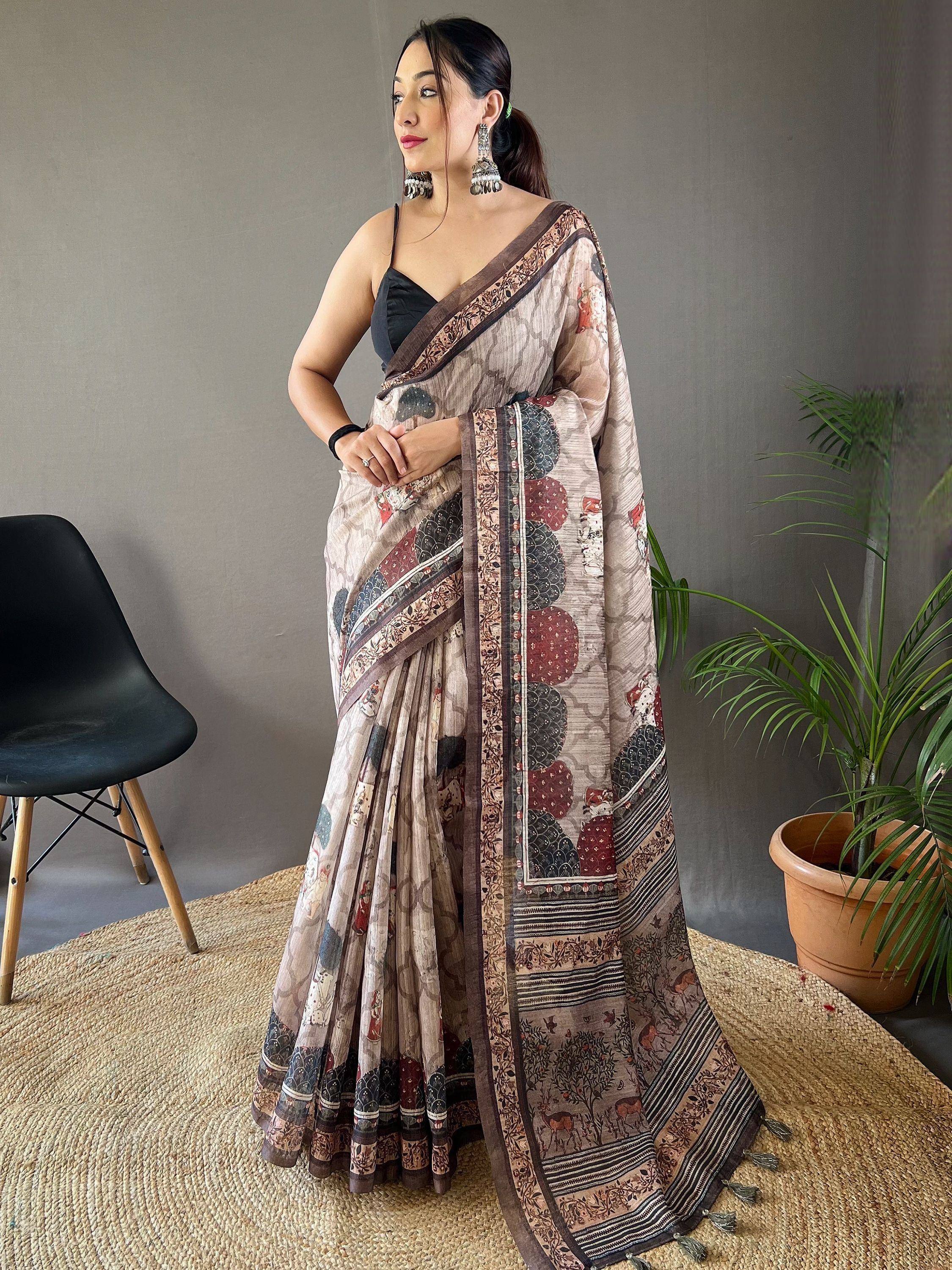 Woman wearing printed ethnic saree with black blouse, traditional jewelry, and tassels, styled for Indian occasions.