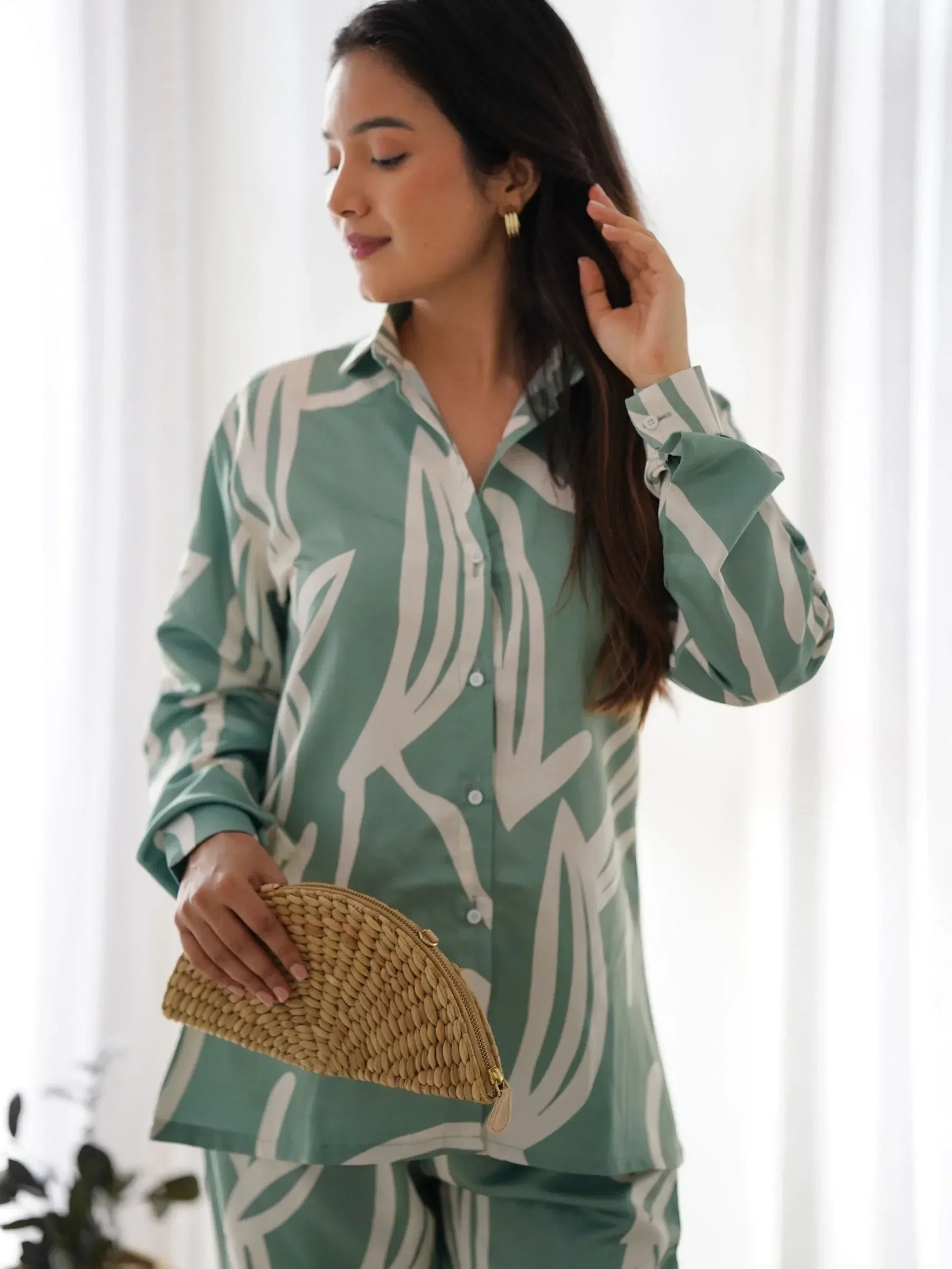 Woman in green and white printed ethnic shirt with ruffled sleeves, holding woven clutch, stylish casual wear