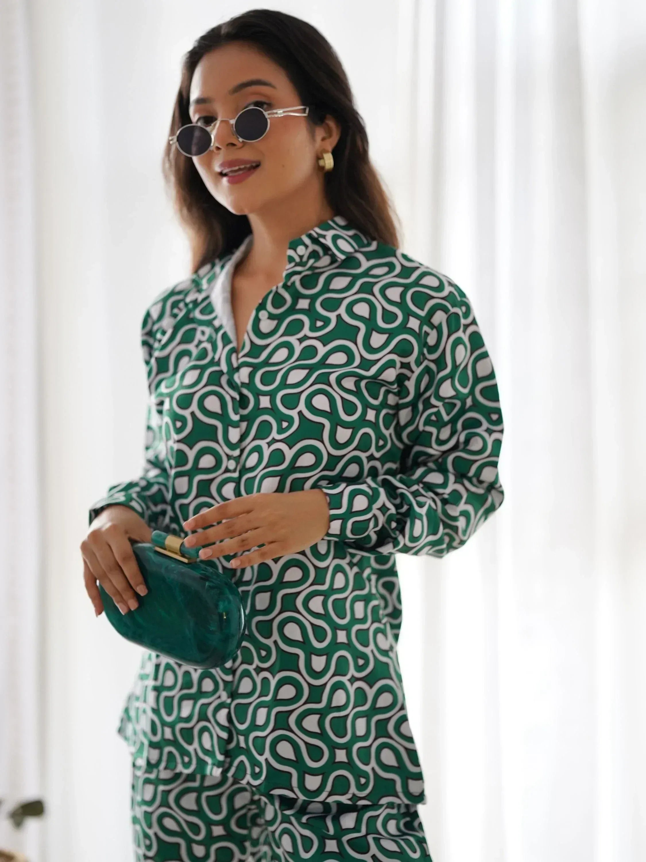 Woman in green and white printed co-ord set, holding a green clutch, wearing sunglasses