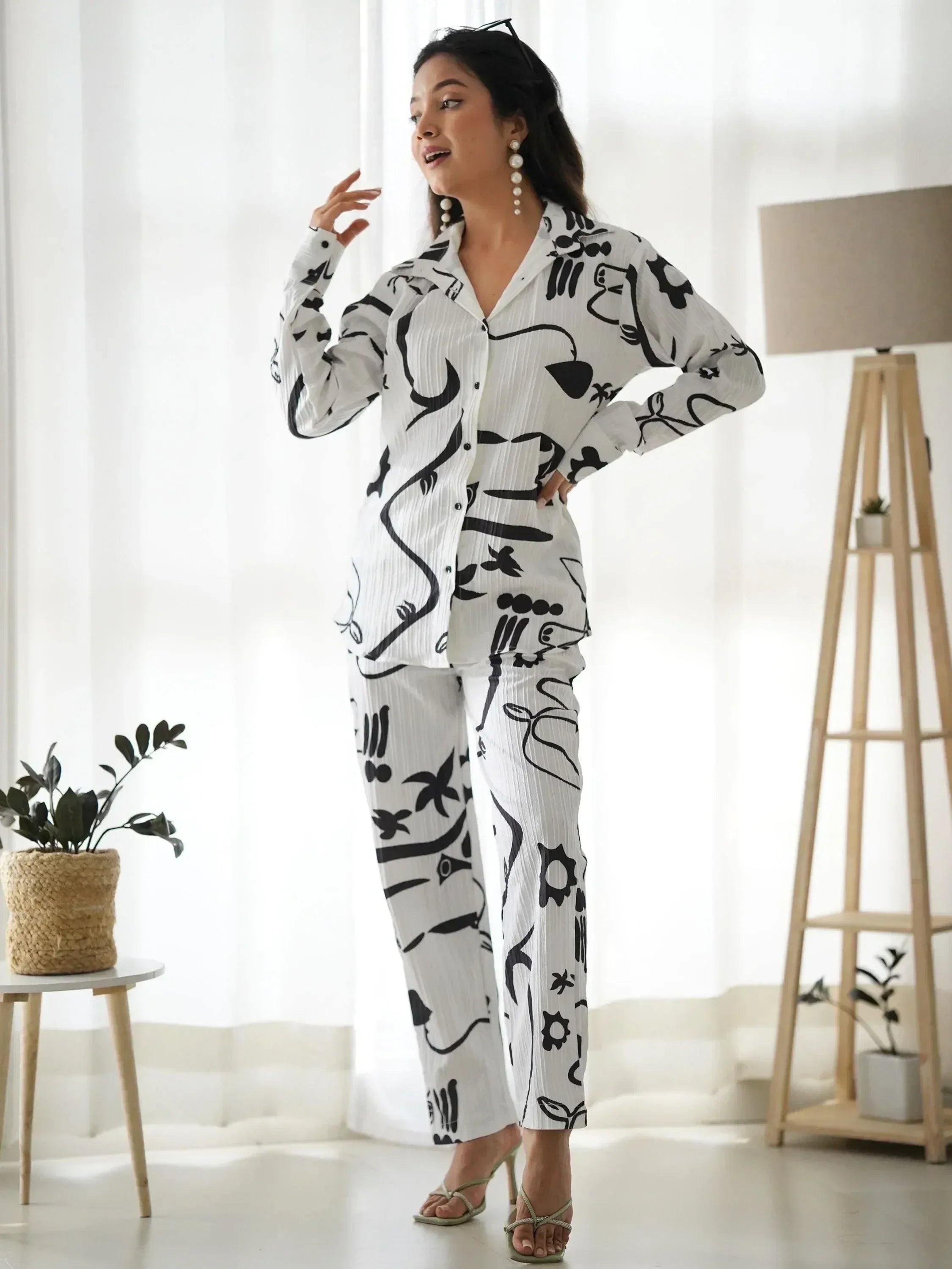 Woman in white and black printed ethnic co-ord set with floral and abstract patterns, styled with heels and pearl earrings.