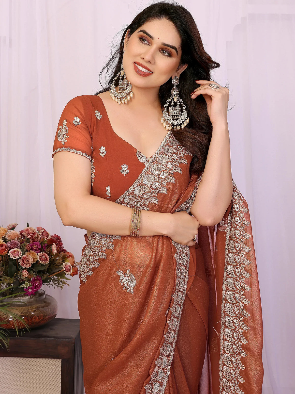 Woman wearing a rust-colored designer saree with intricate silver embroidery and heavy earrings