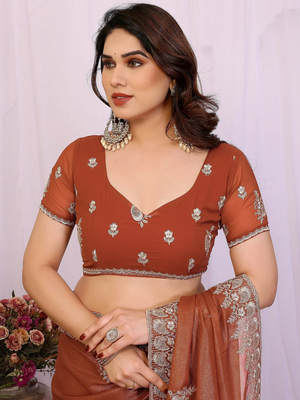 Woman wearing a rust-brown designer lehenga choli with silver embroidery and ethnic jewelry.