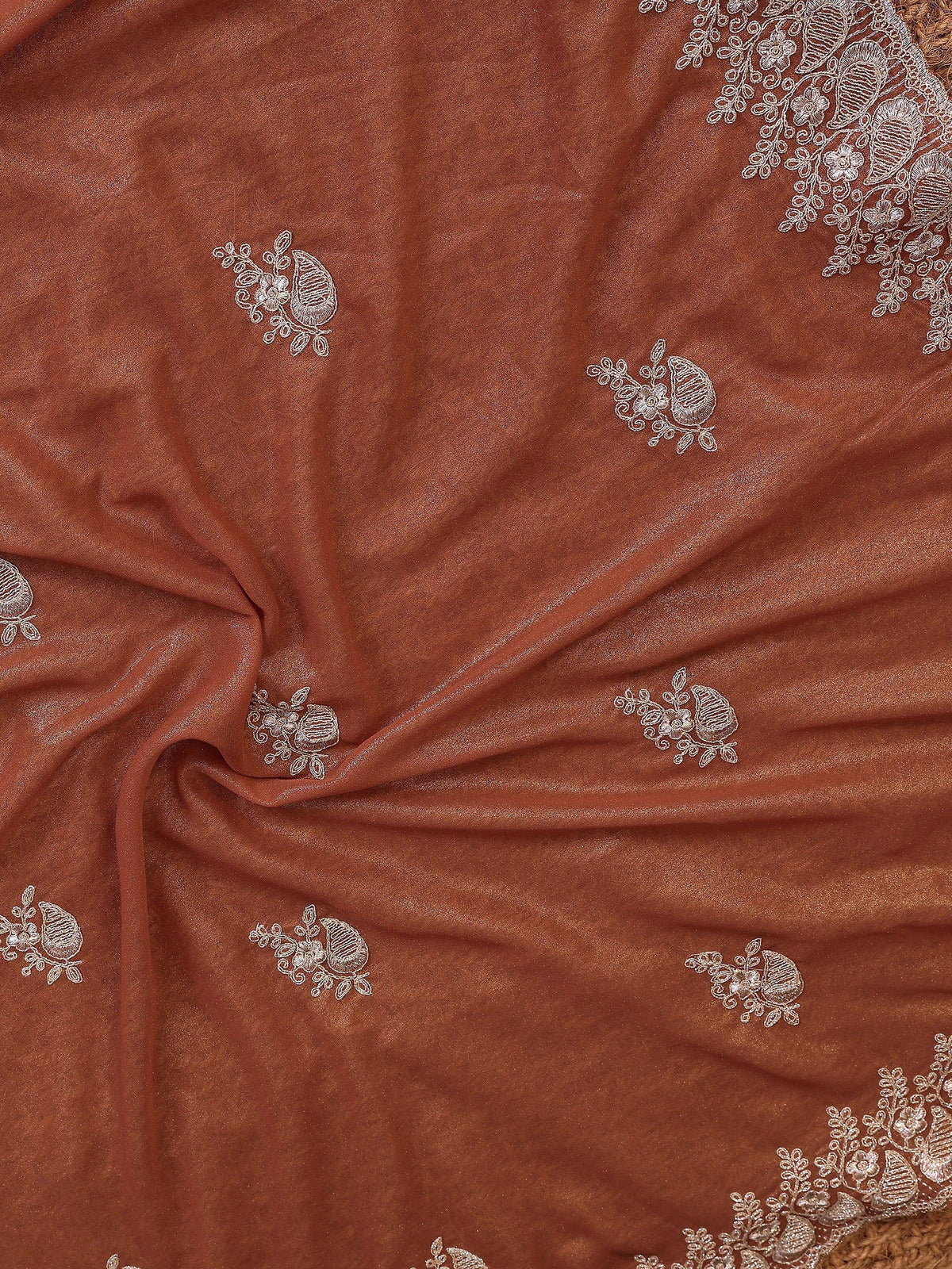 Close-up of rust-colored ethnic saree fabric with delicate silver floral embroidery