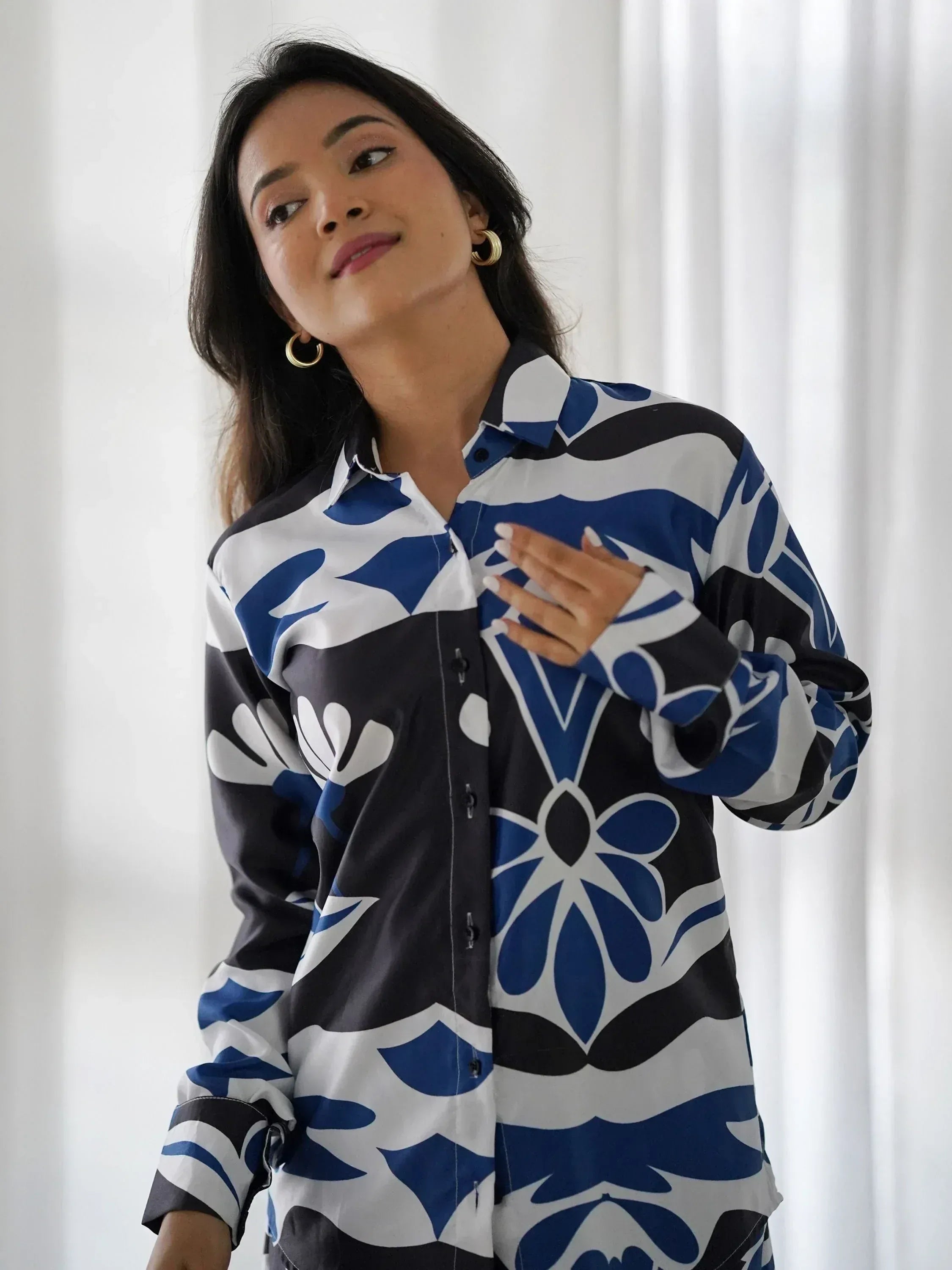 Woman wearing blue, white, and black floral print shirt dress with gold hoop earrings