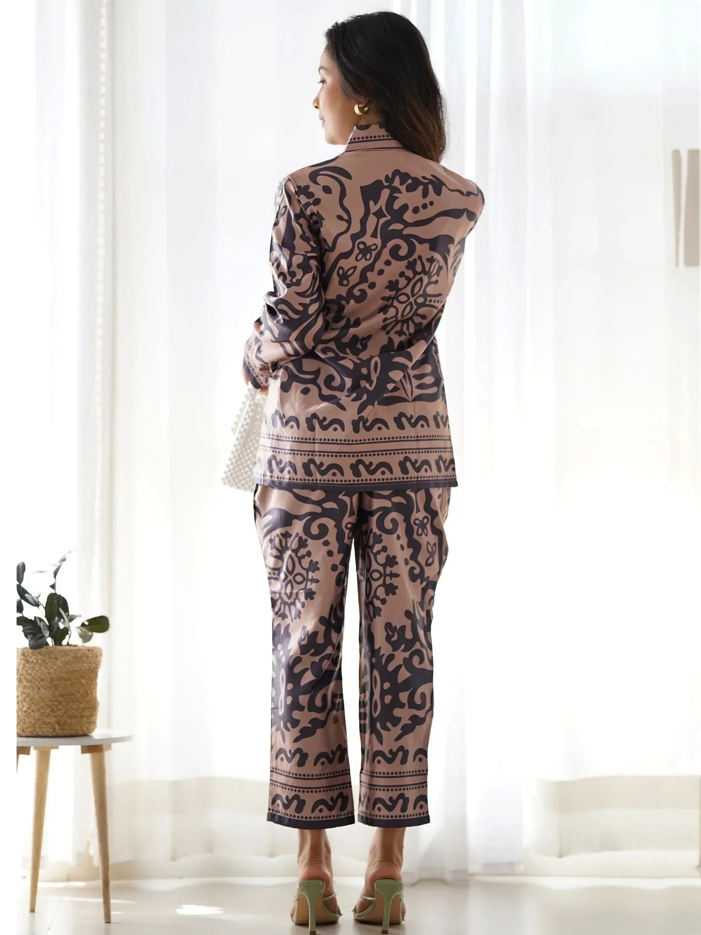 Woman in elegant ethnic print pajama set with high collar, standing by window, showcasing designer loungewear
