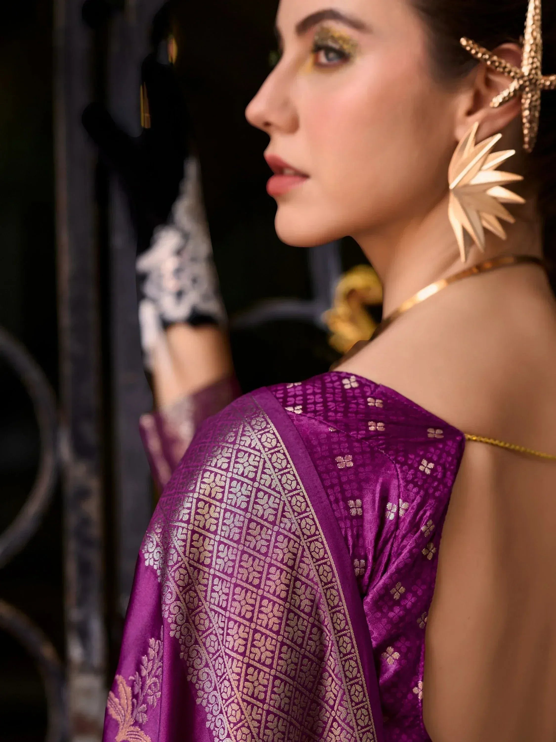 Purple ethnic saree with gold floral weave, off-shoulder drape, and statement gold jewelry for festive occasions