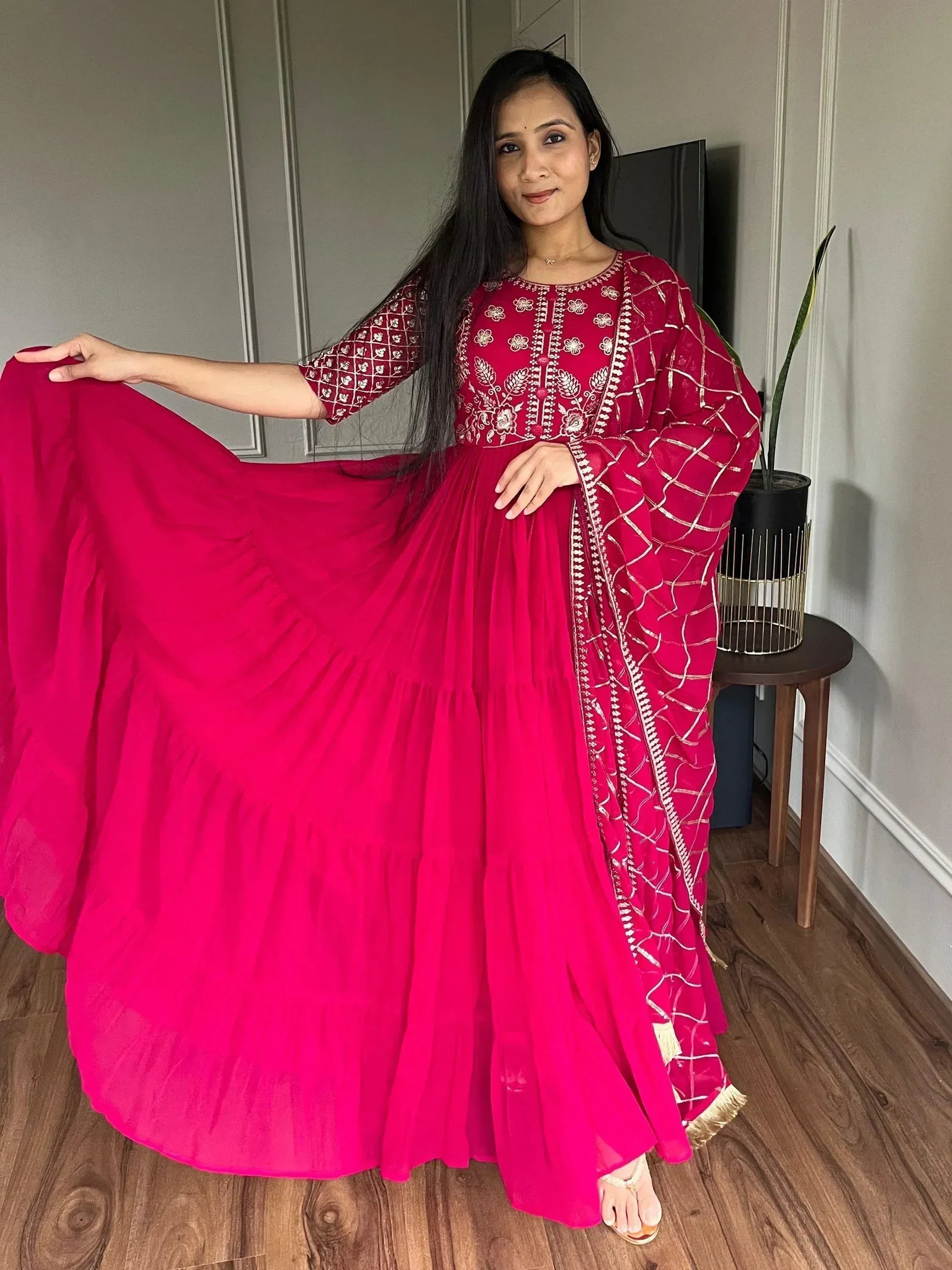 Woman in vibrant pink embroidered ethnic gown with flared skirt and gold detailing, perfect for festive occasions.