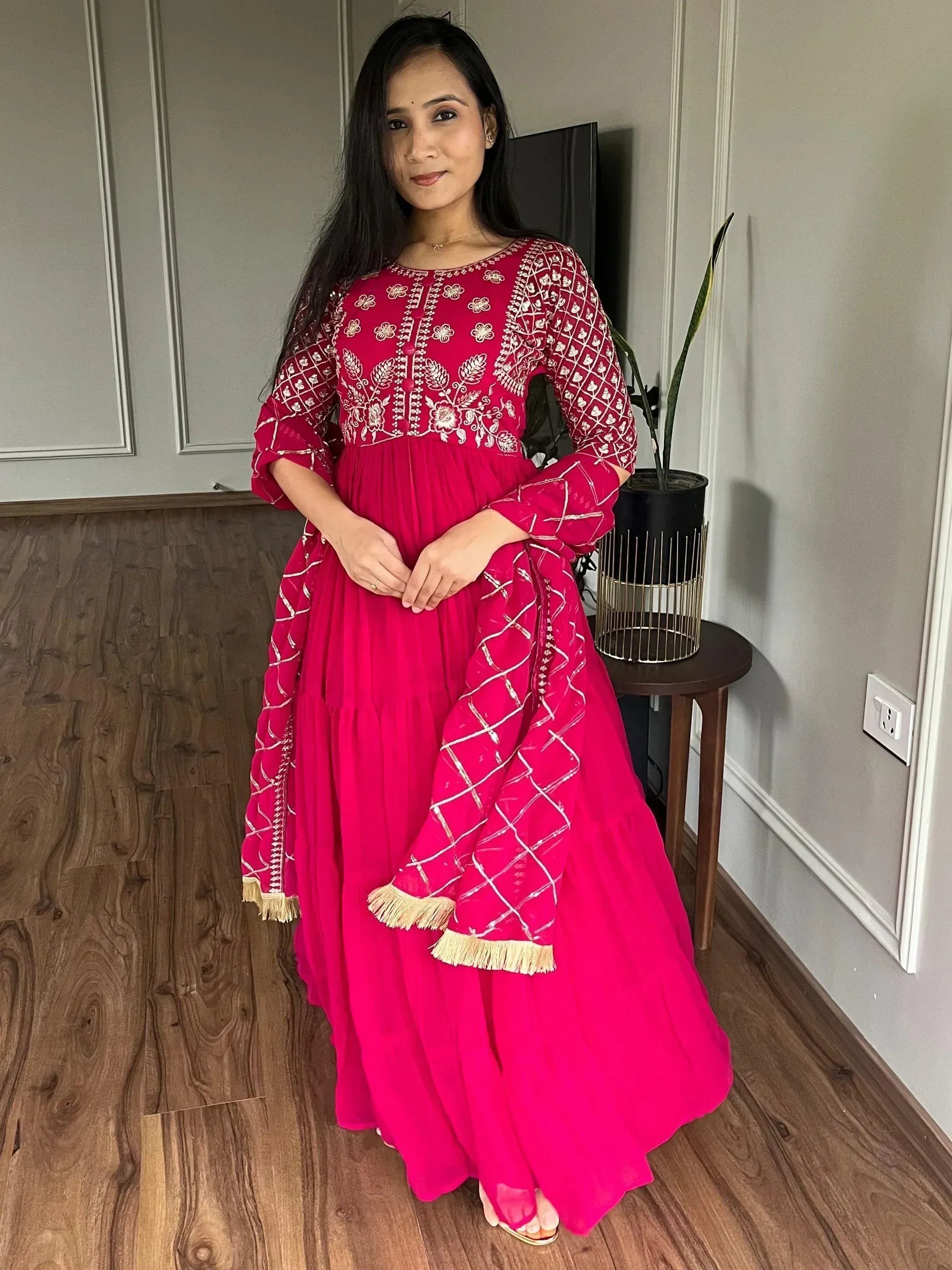 Vibrant pink ethnic gown with white embroidery and gold fringe, perfect for Indian festive occasions.