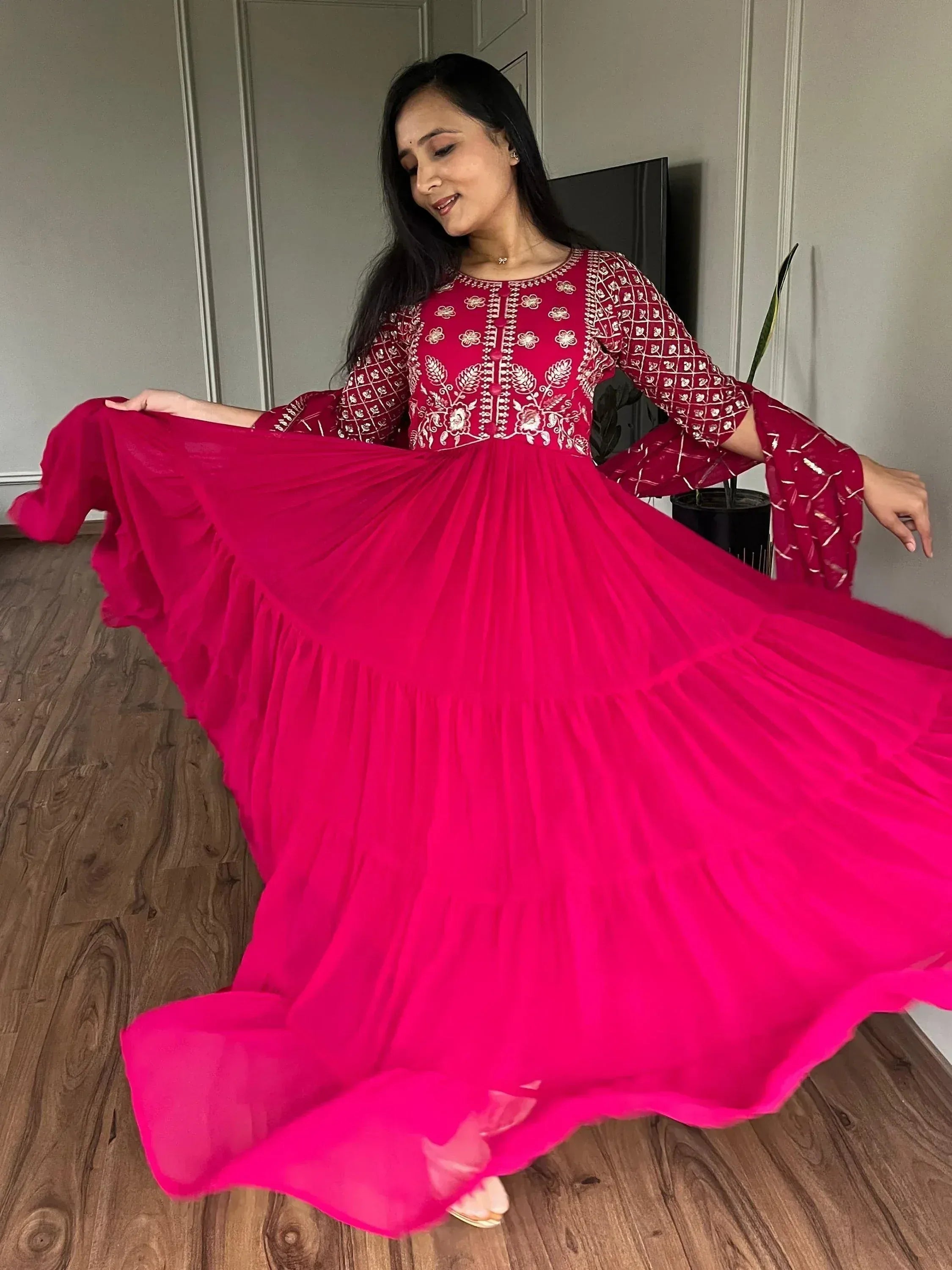 Woman in vibrant pink ethnic gown with floral embroidery, twirling gracefully indoors