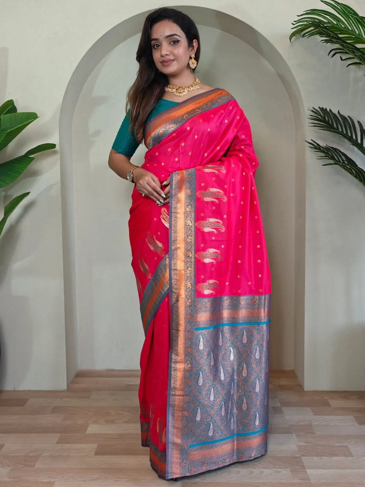Vibrant pink and red designer saree with gold motifs and blue border, paired with teal blouse for ethnic wear